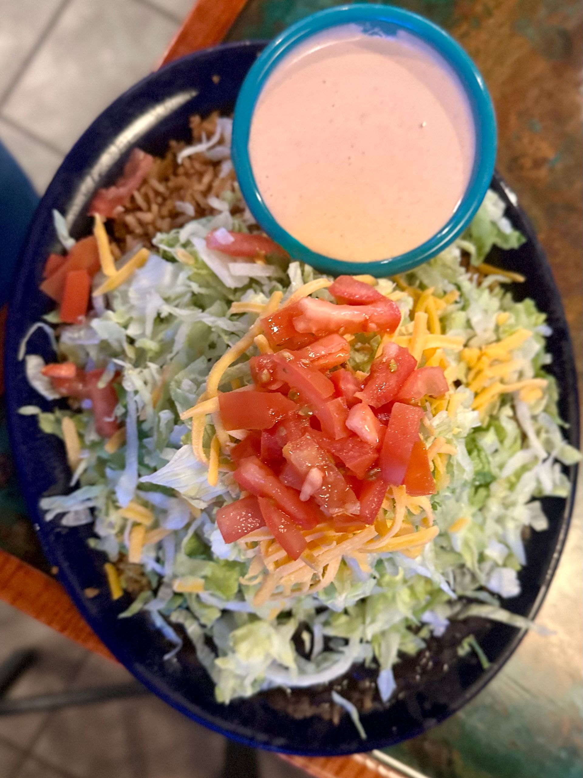 Taco salad: shredded lettuce, tomatoes, cheese, meat, and pink sauce in a blue bowl.