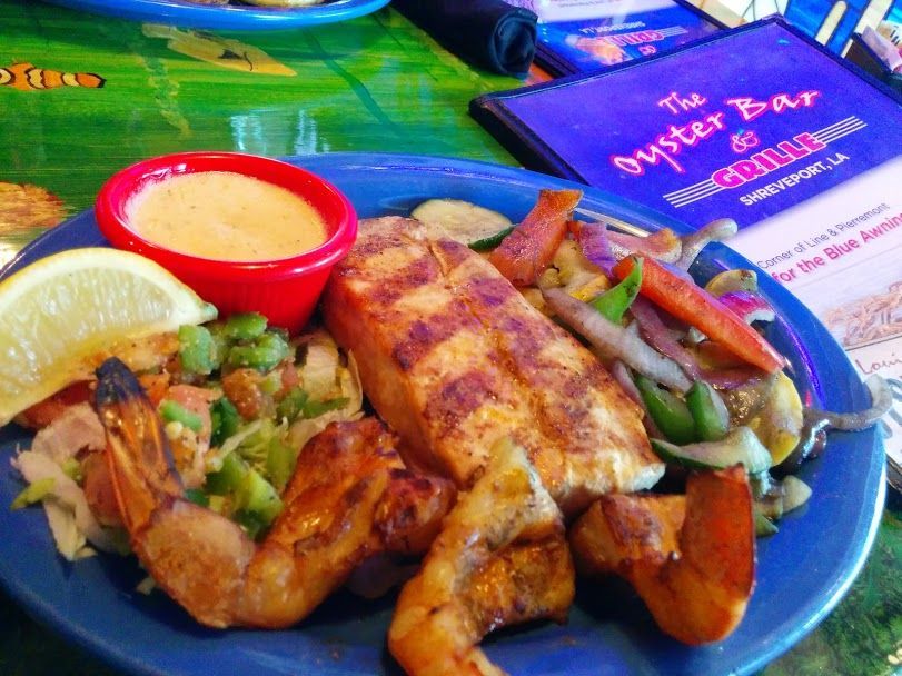 Grilled salmon and shrimp plate with vegetables and sauce, on a blue plate at a restaurant.
