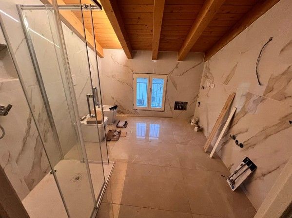 Bagno con pareti in marmo beige, doccia, travi in ​​legno e finestra.