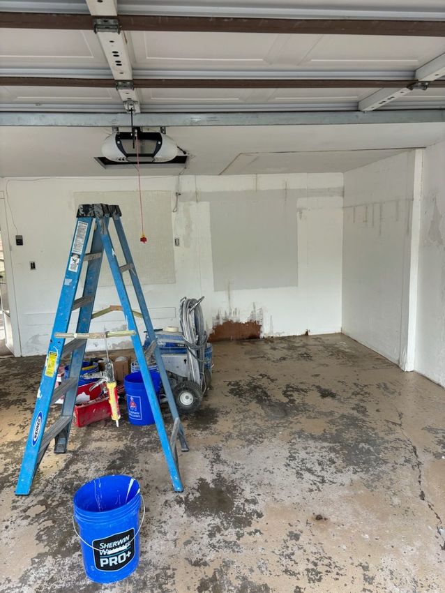 An empty garage with a blue bucket and a blue ladder