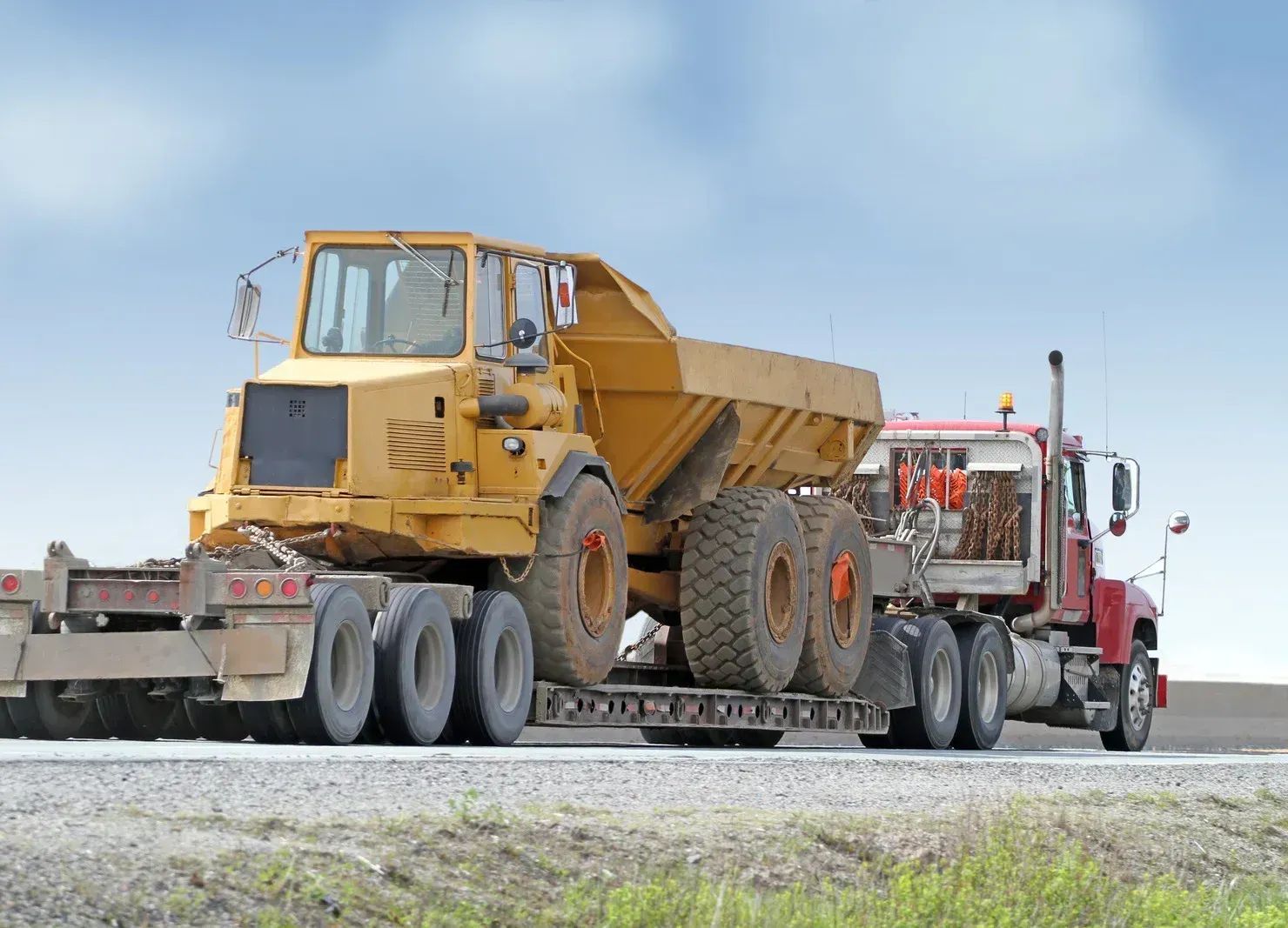 A semi truck is carrying a large yellow dump truck on a trailer.