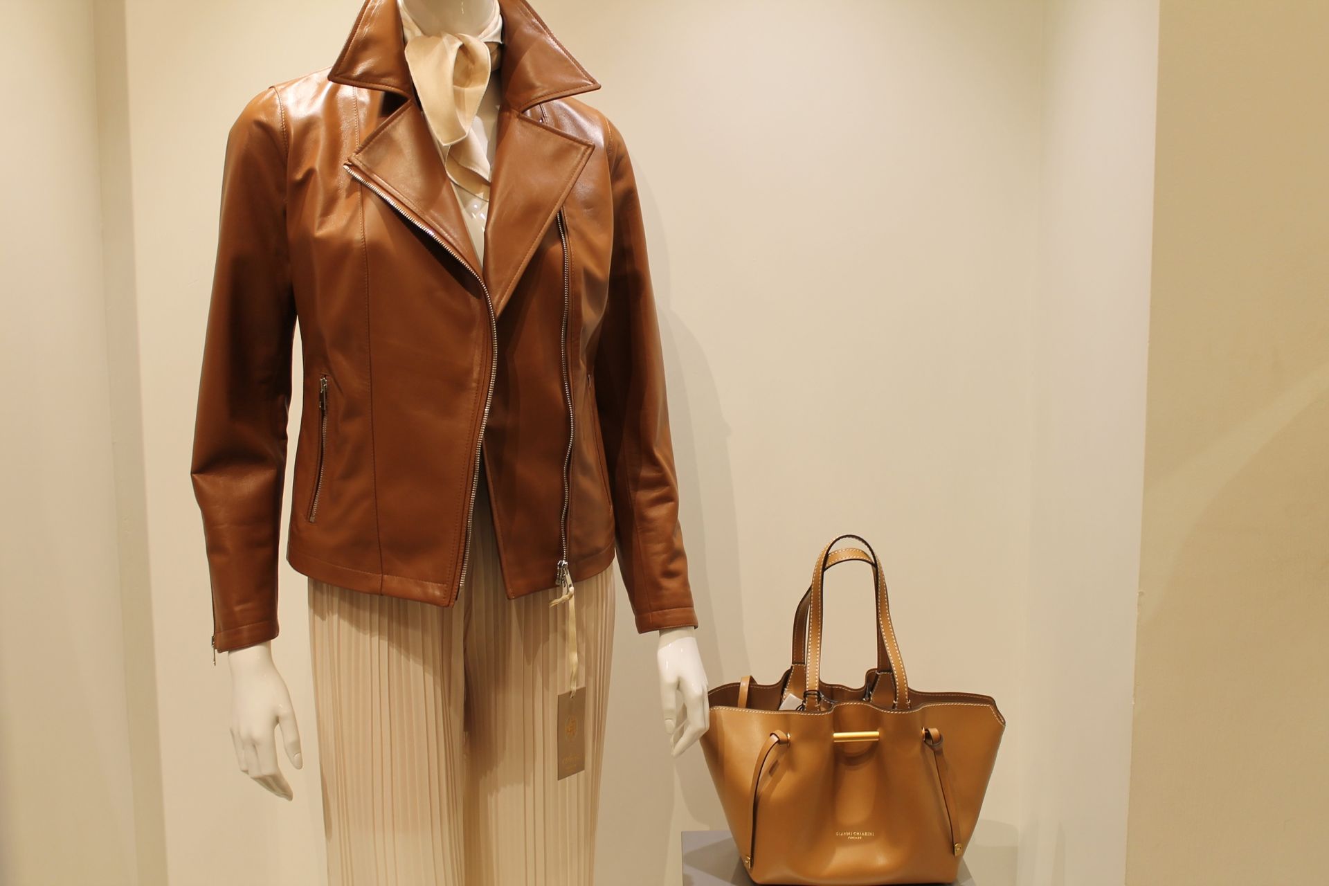 Una giacca di pelle marrone è su un manichino accanto a una borsa marrone.