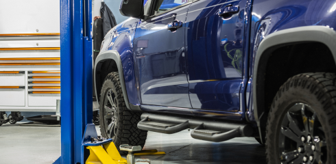 A close-up of a blue pickup truck raised on a mechanic's lift inside a professional workshop. | Airpark Auto Pros