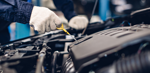 A mechanic wearing white gloves checks the engine oil level with a dipstick in a car engine bay. | Airpark Auto Pros