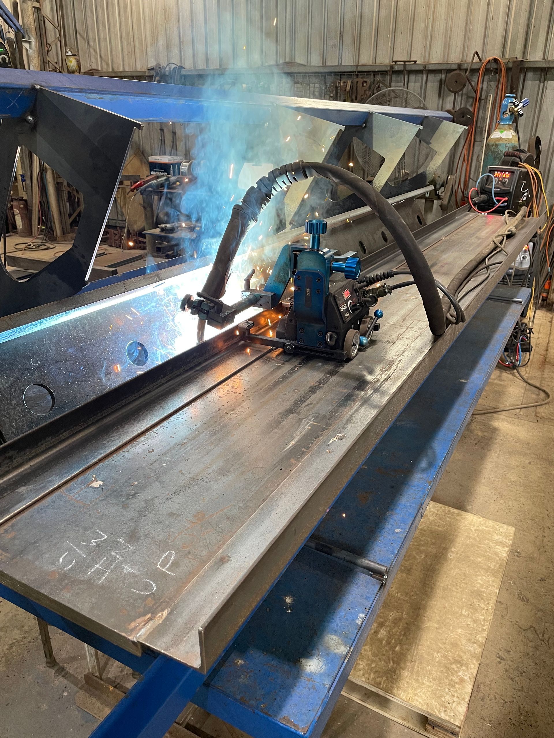 A Man Is Working On A Large Blue Metal Structure In A Factory — Primmer Steel In Nabiac, NSW