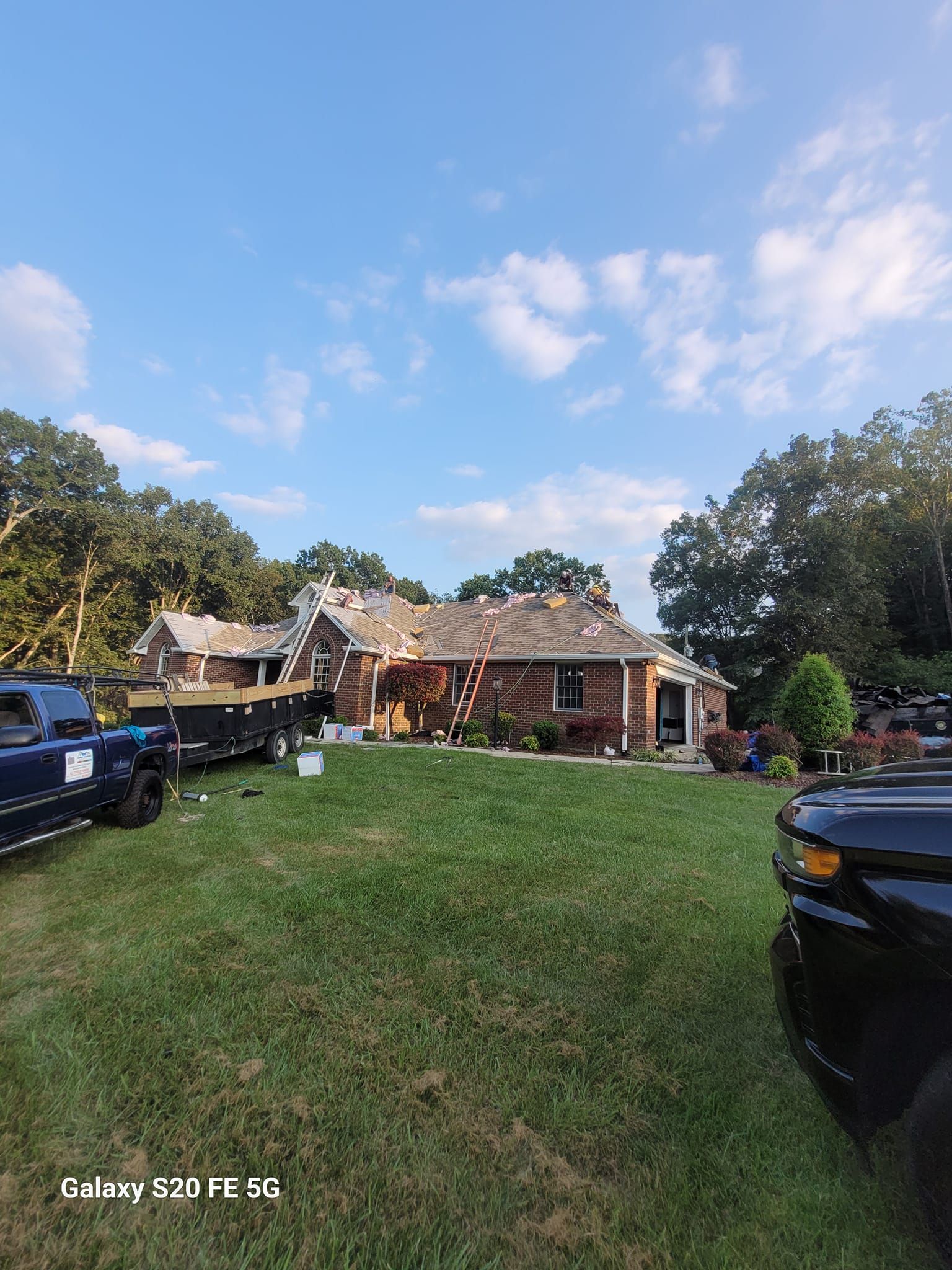 House with partially removed roof, construction vehicles, and green lawn under a blue sky.