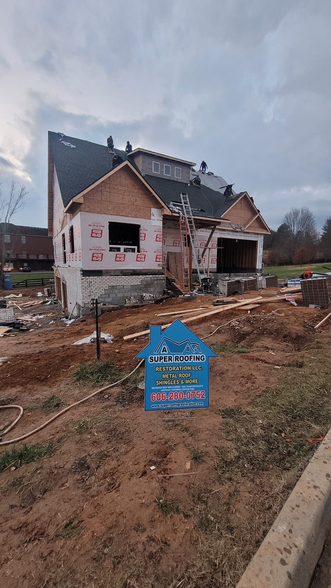 A partially built house with exposed wood framing, sheathing, and roofing material; a blue sign in front.