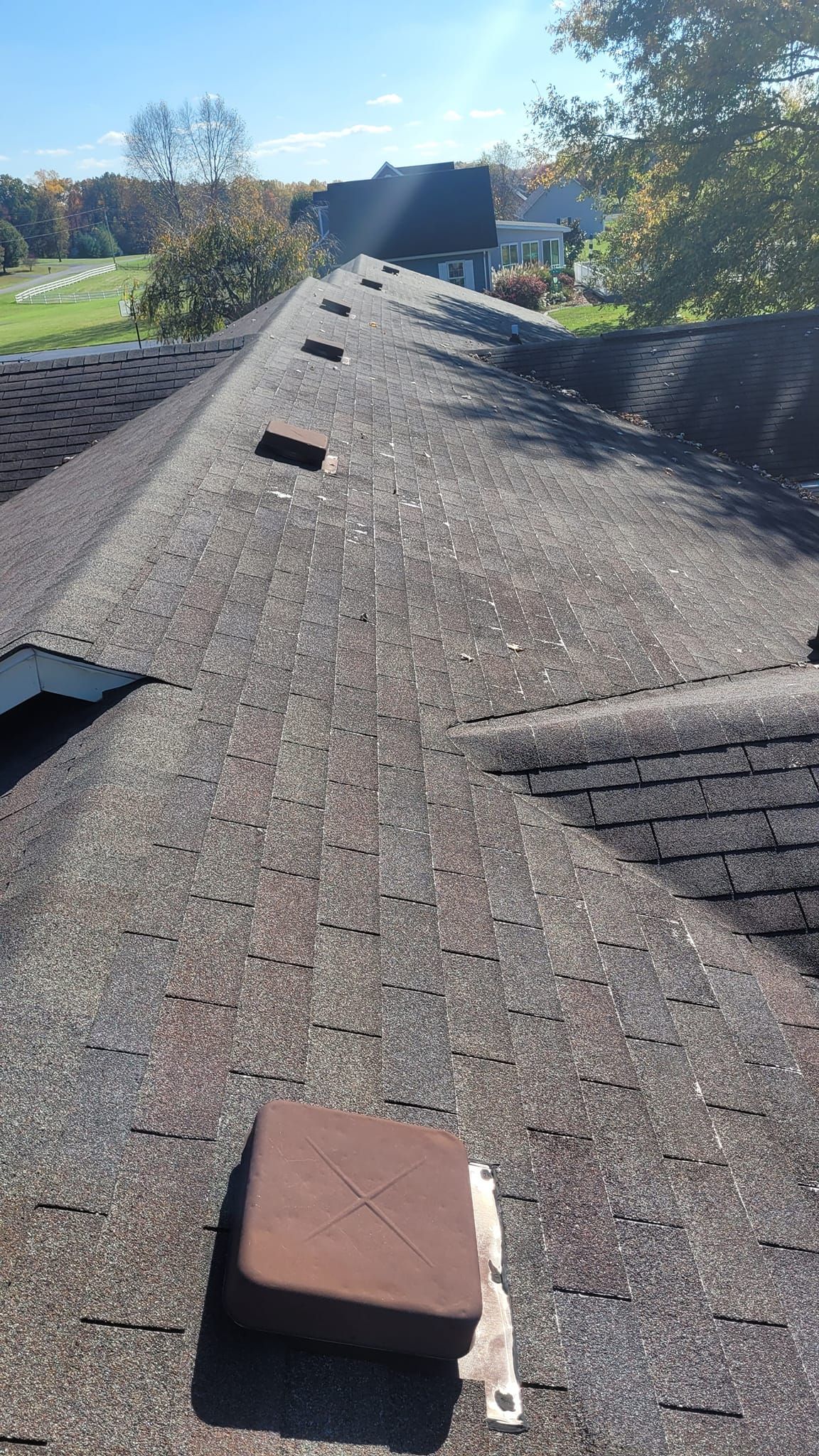 View of a weathered asphalt shingle roof, with debris and a brown square object on it, under a blue sky.