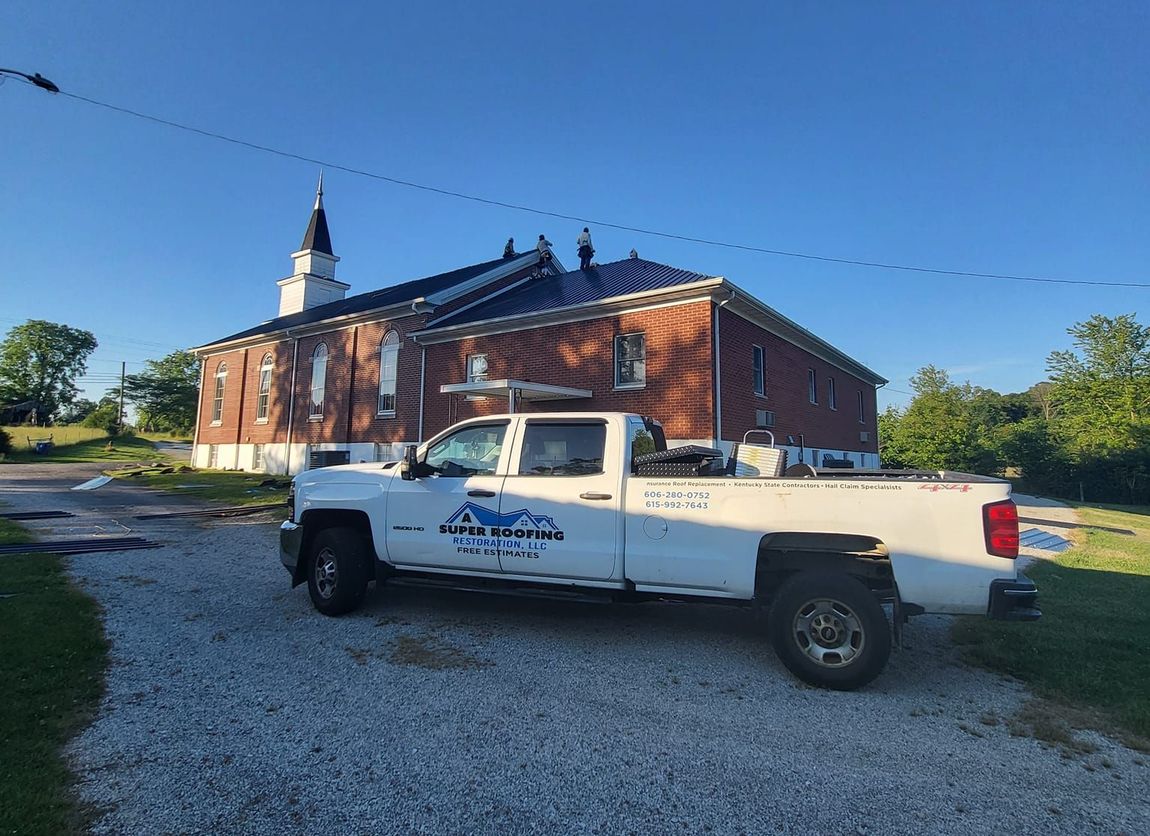 White work truck parked in front of a brick building with blue roof and steeple.