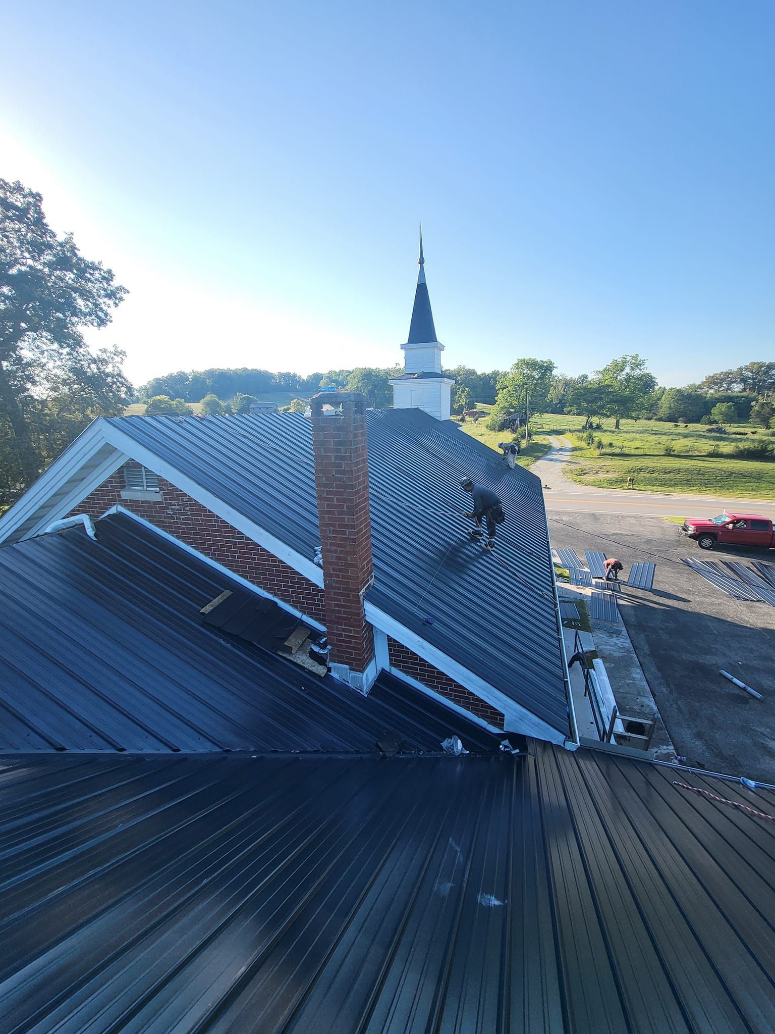 Church roof with chimney, steeple in the distance, sunny day.