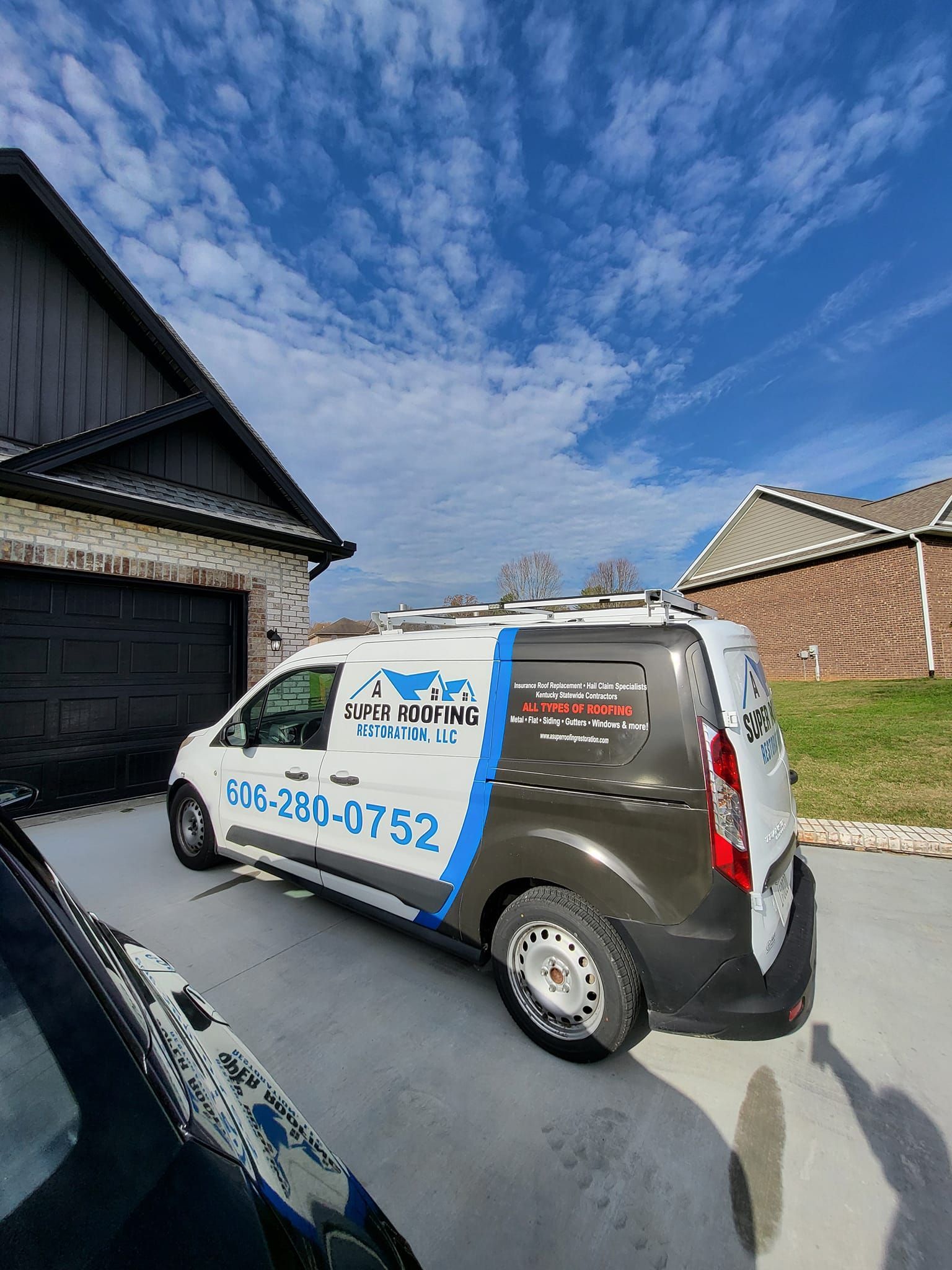 White and black service van with phone number parked next to a house with a blue sky background.