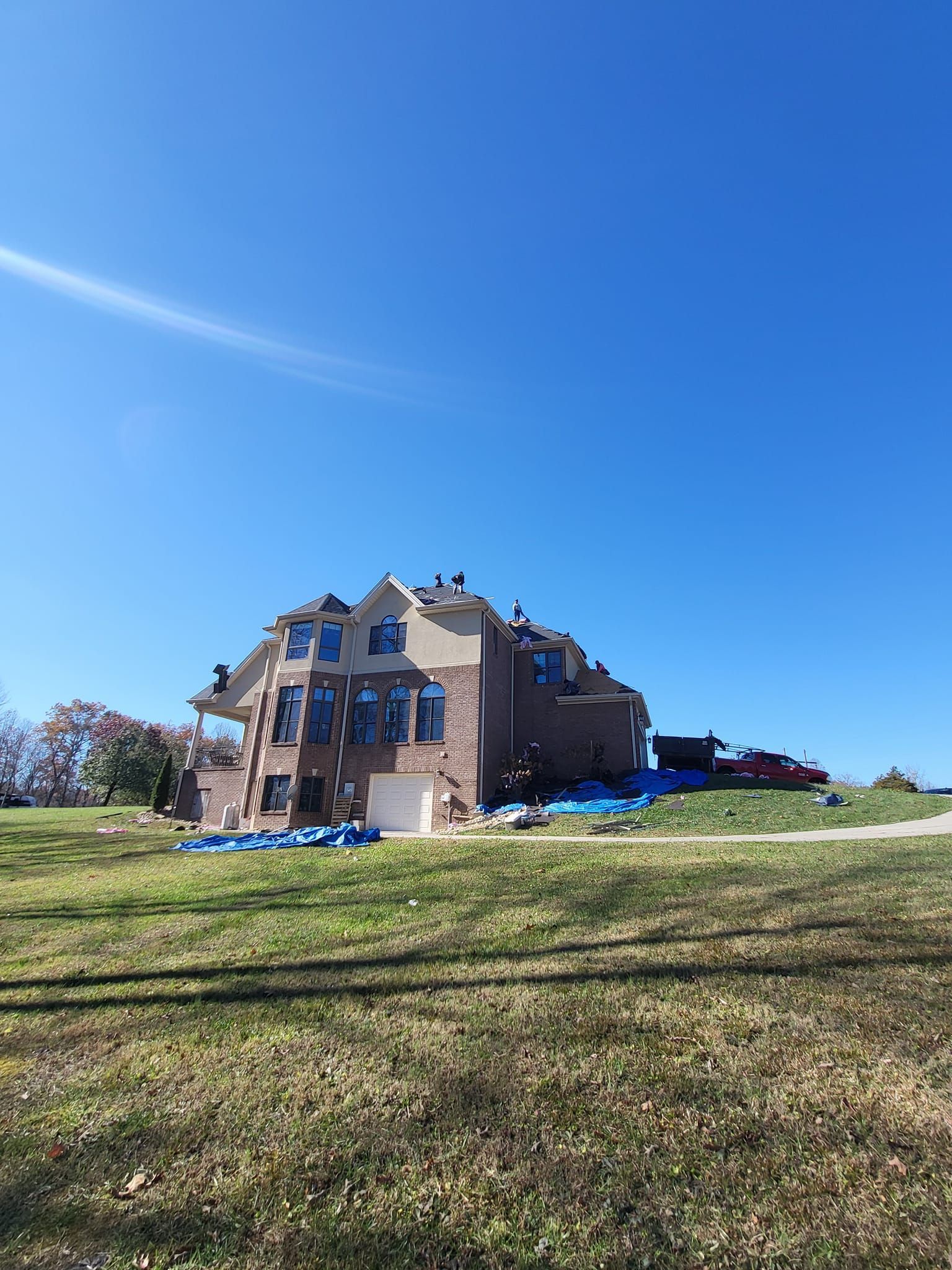 House with roofing work in progress on a grassy hill, bright blue sky above.