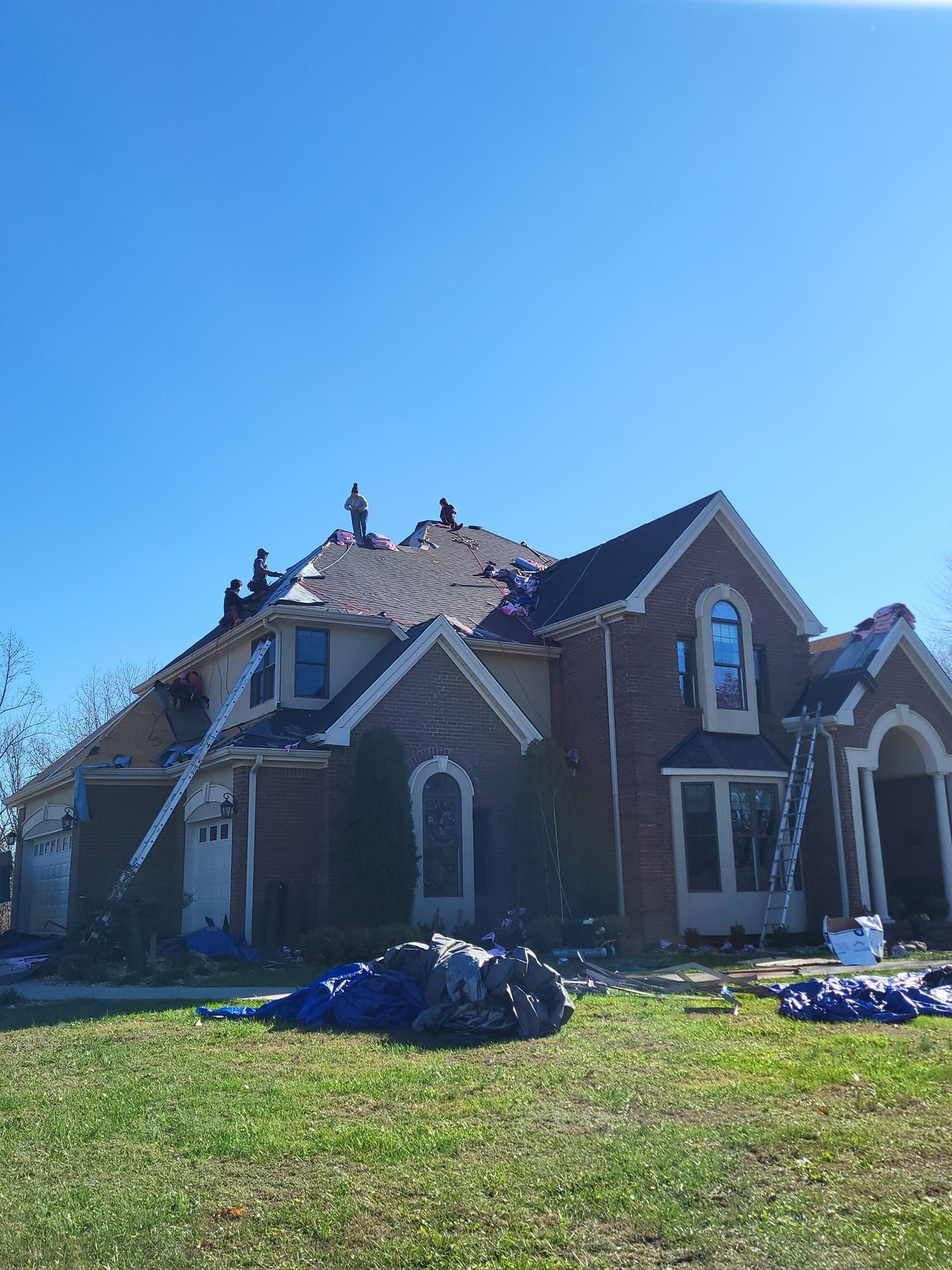 House with partially removed roof, blue tarp, ladders, and yard.