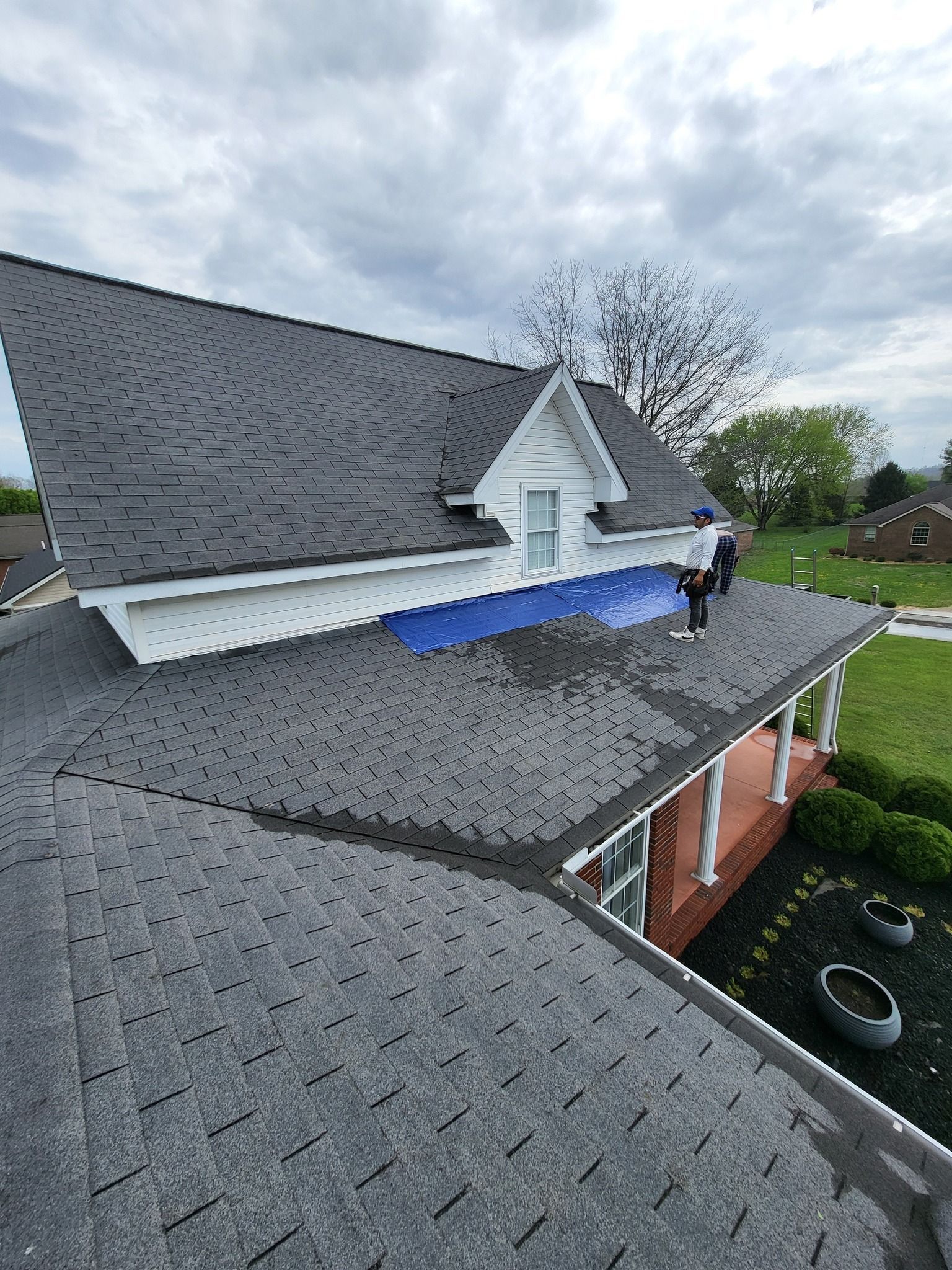 House roof with gray shingles, white trim, and a blue tarp. Overcast sky.