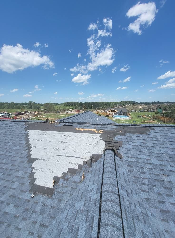 Damaged roof with missing shingles against a blue sky with scattered clouds.