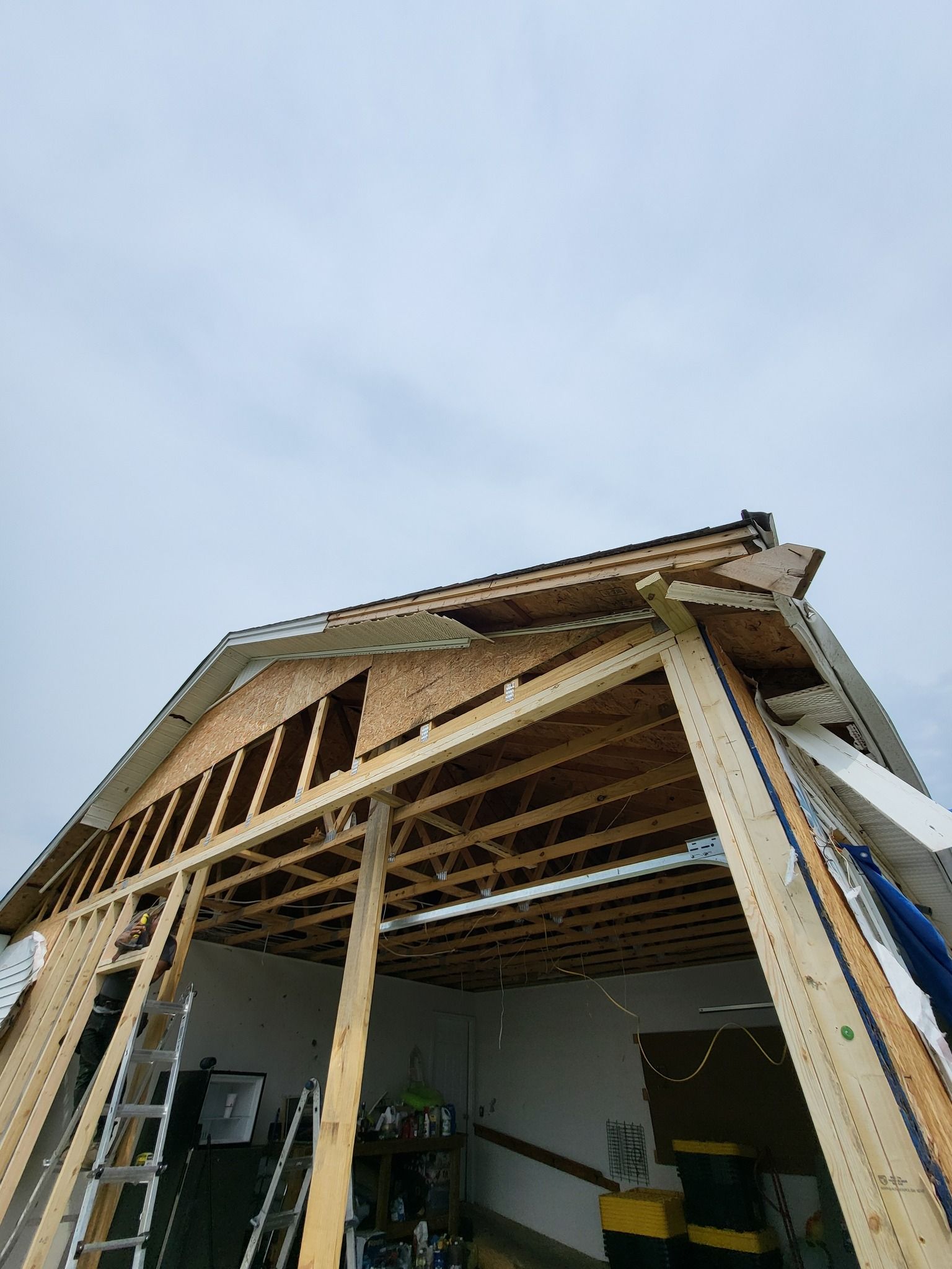 Construction of a gable roof, partially framed, over a garage. Blue sky in the background.