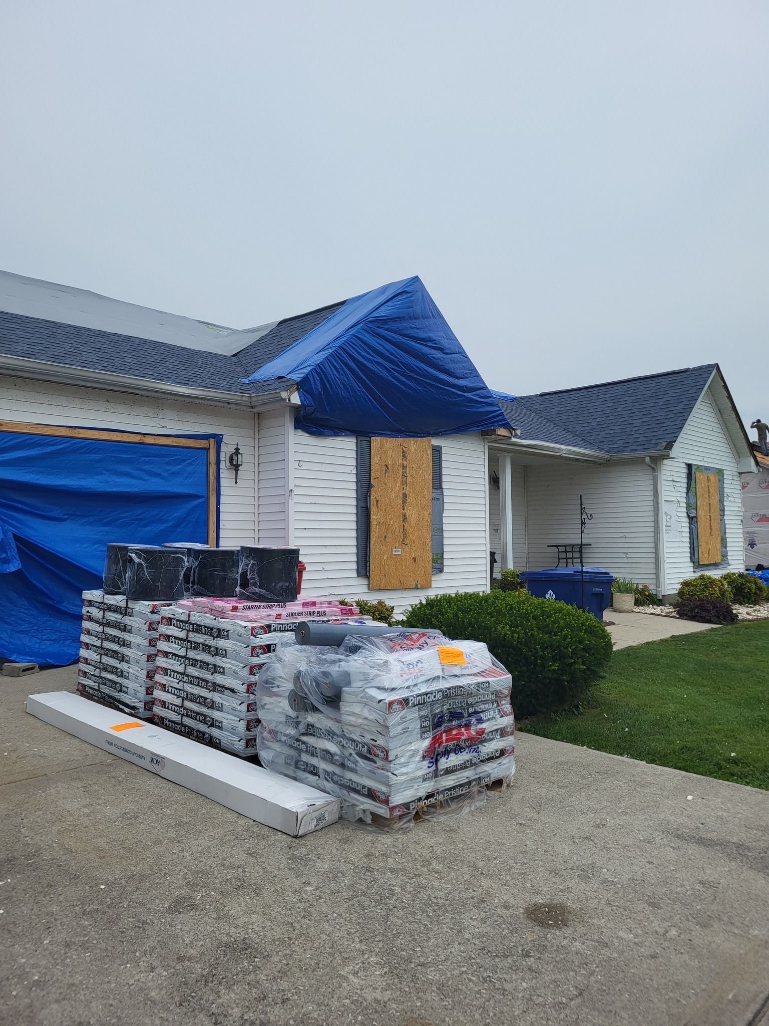 House under construction, covered in blue tarps, with building materials stacked on driveway.