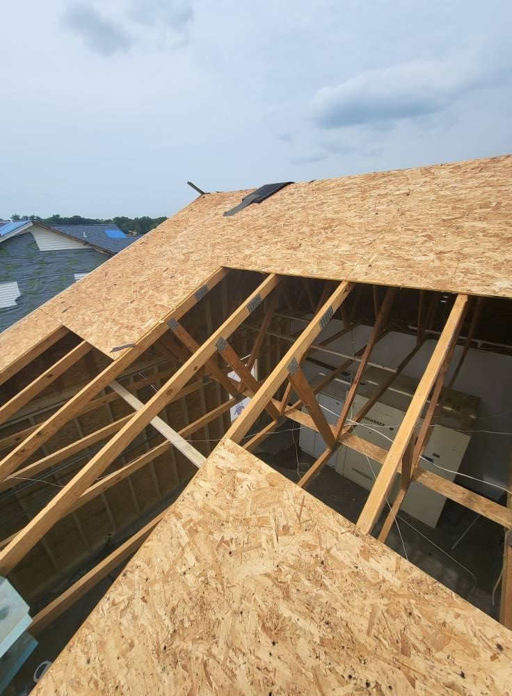 Construction of a roof. OSB sheathing covers exposed wooden rafters. Open area reveals interior framing. Sky visible.