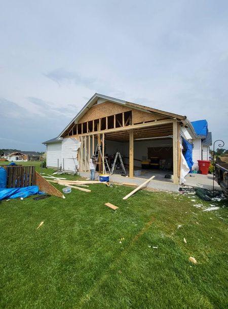 Garage addition under construction on a house, lumber and tools visible on the lawn.