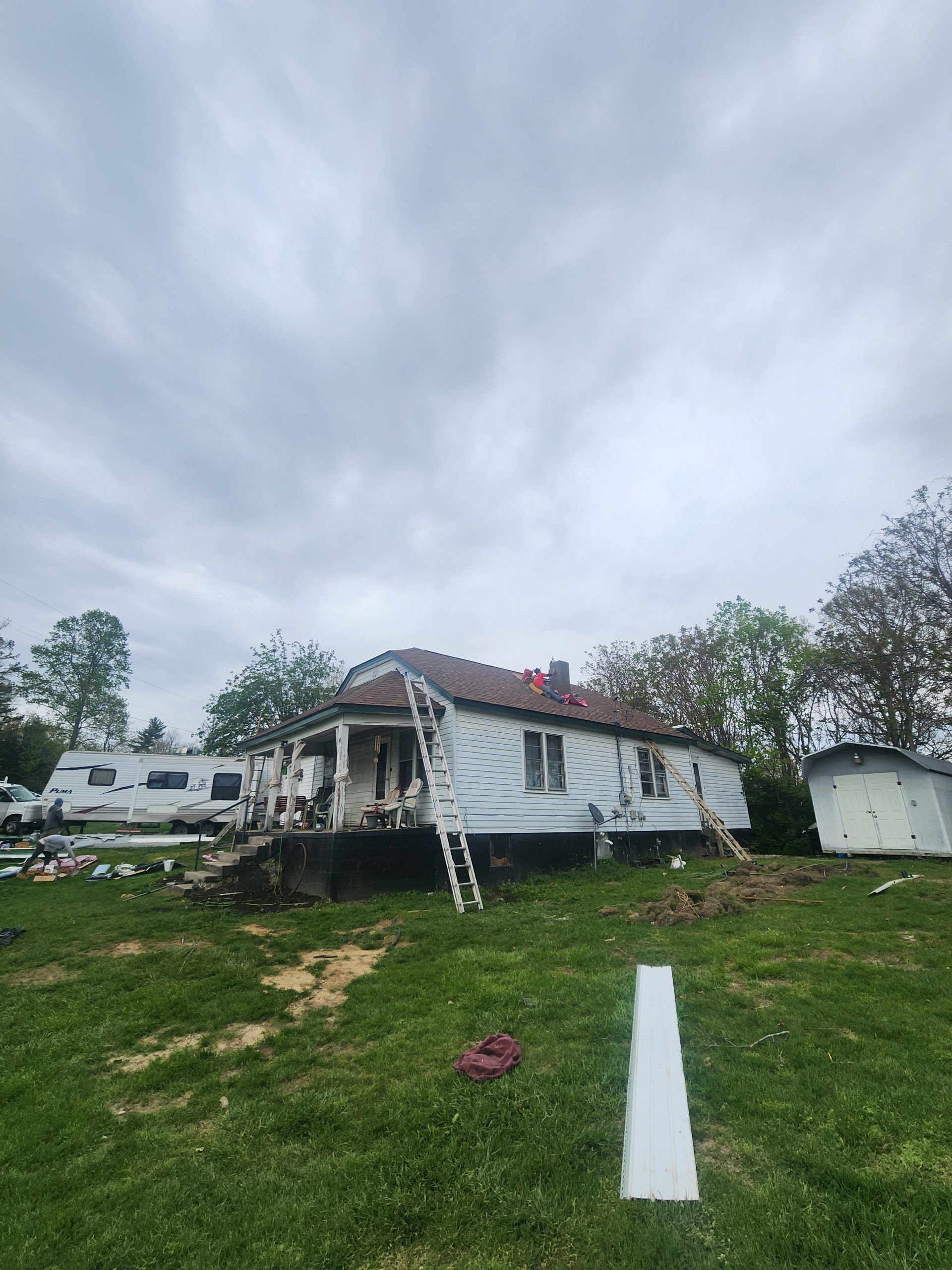 House under construction with ladders and a trailer, cloudy sky overhead.