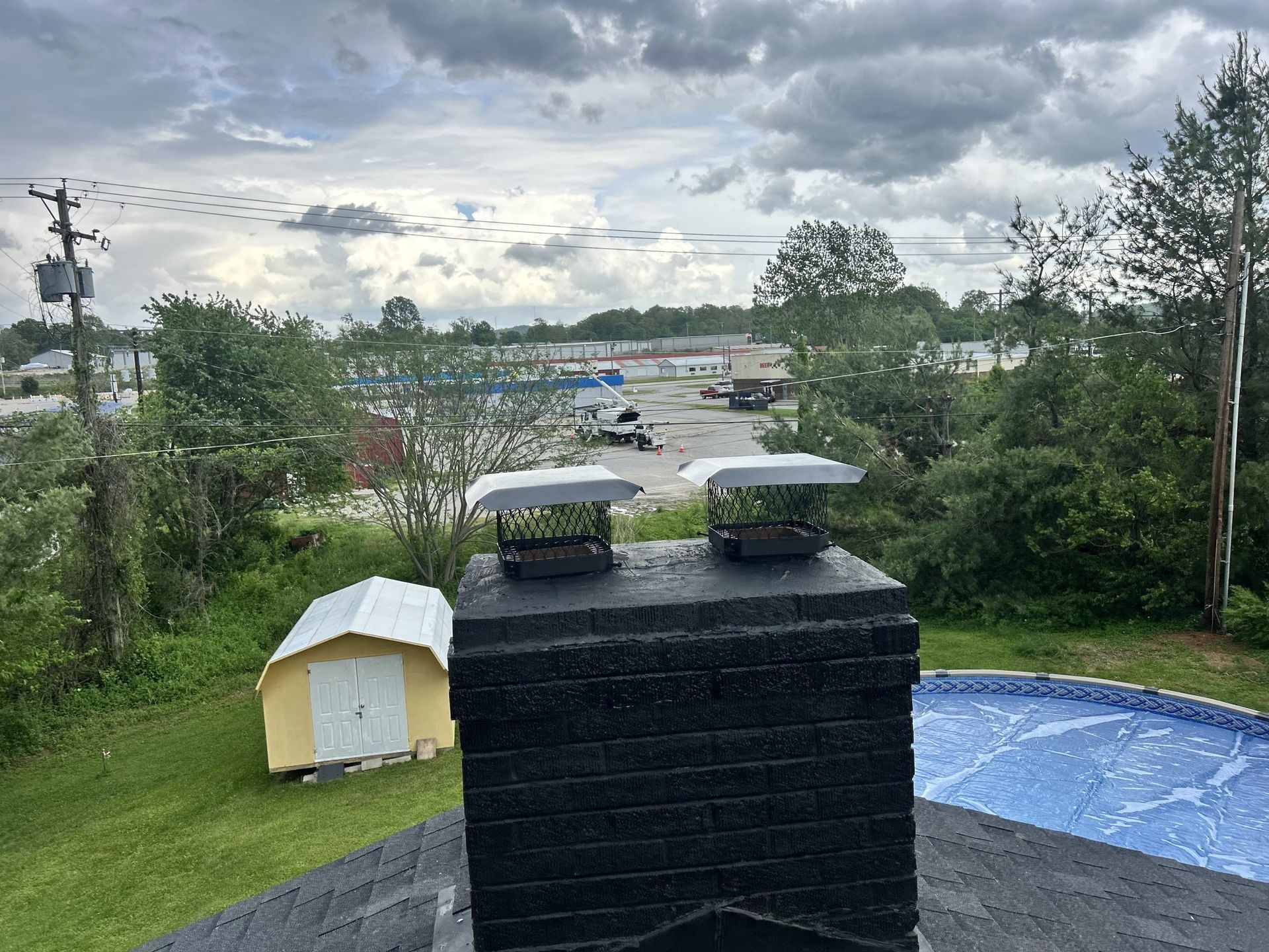 Black brick chimney on a roof with metal caps, overlooking a green landscape and cloudy sky.