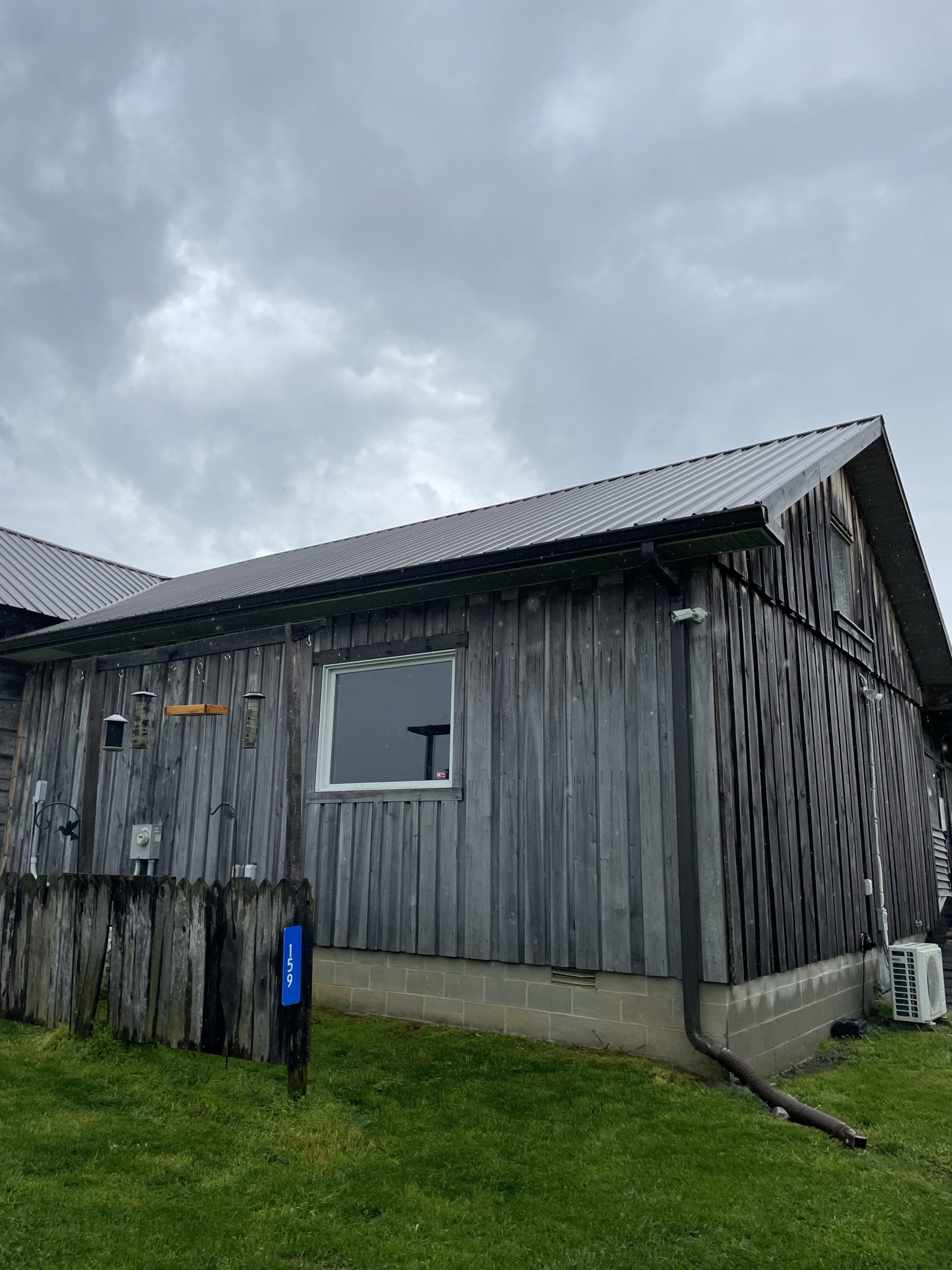 Weathered wooden building with a dark roof and small window against a cloudy sky.