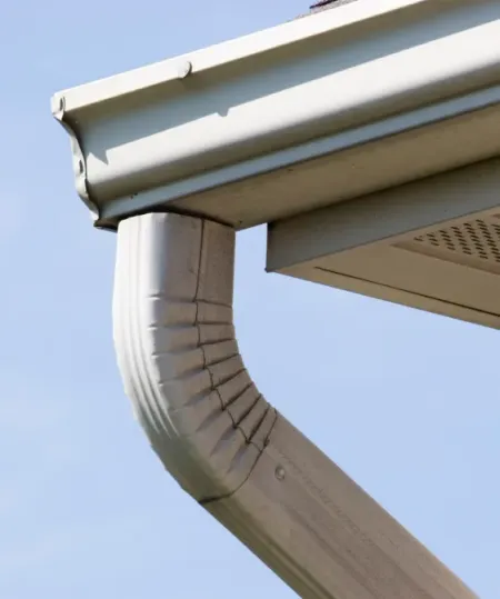 White gutter and downspout on a building exterior, angled against a light blue sky.
