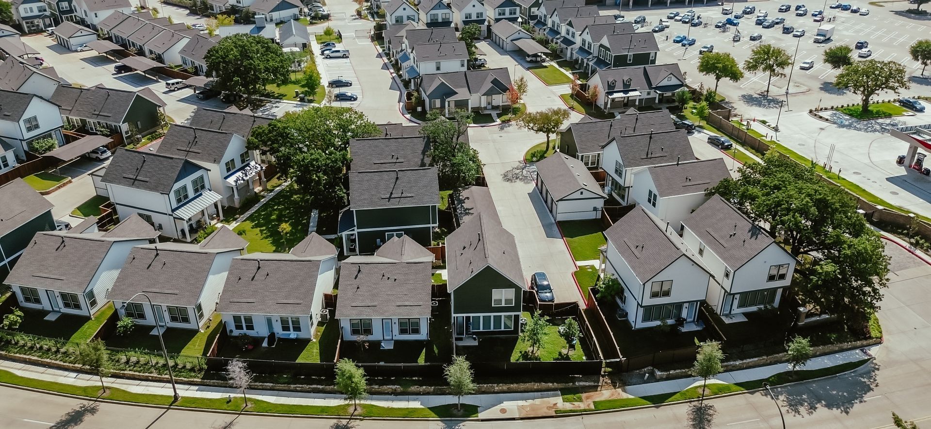 Aerial view of a suburban neighborhood with rows of houses, trees, and parking area.
