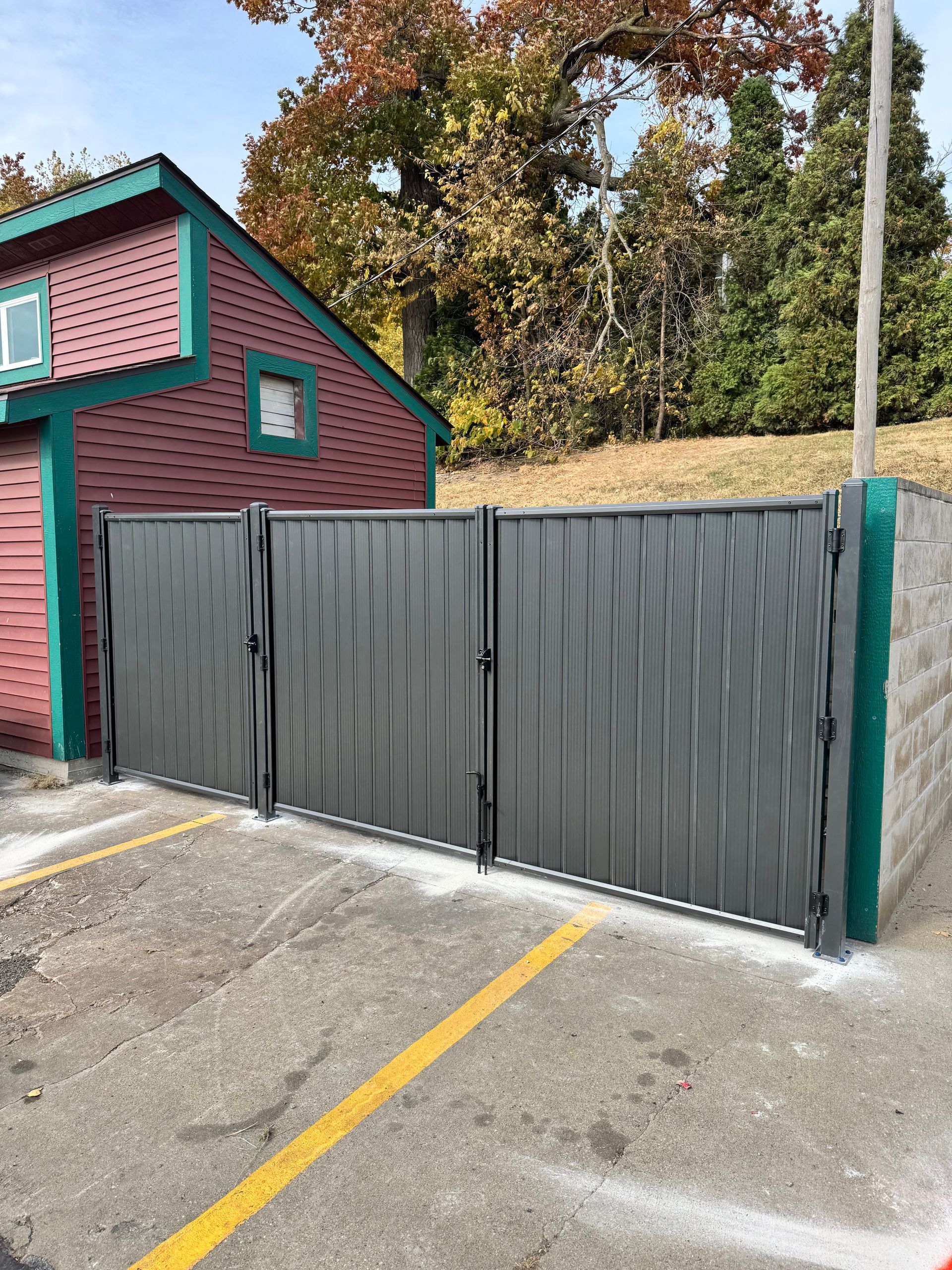 Black fence curves along a grassy yard, with trees on the left and a cloudy sky in the background.