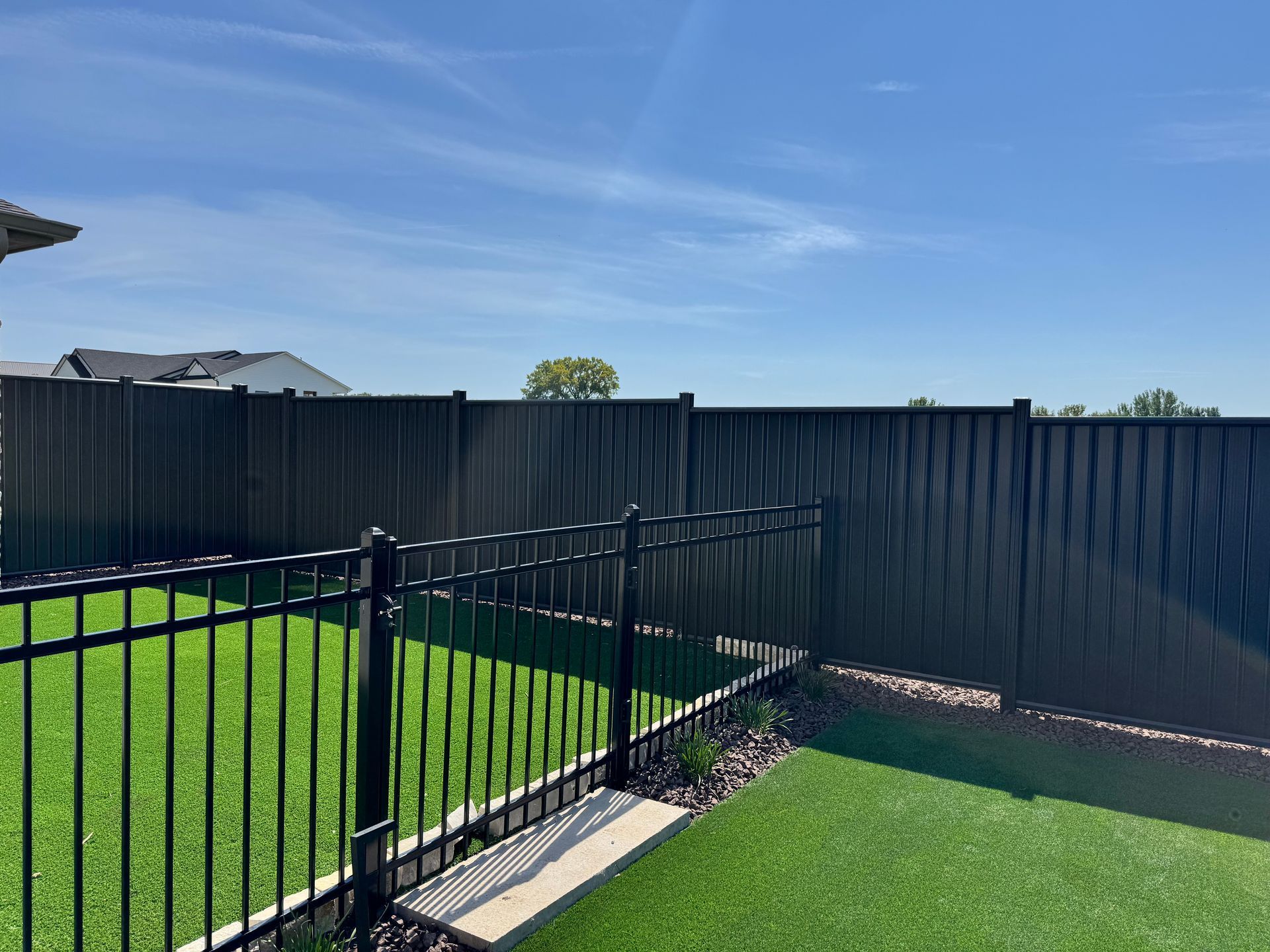 Black fence curves along a grassy yard, with trees on the left and a cloudy sky in the background.