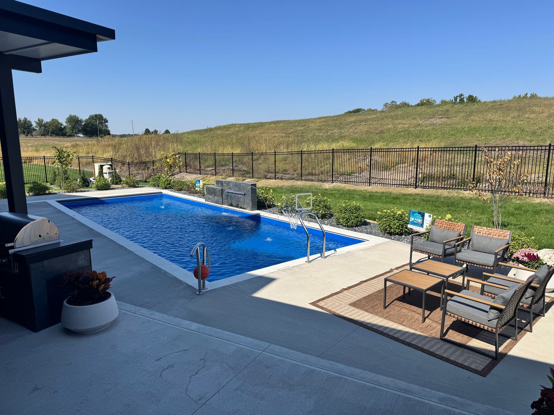 Black metal fence surrounding a backyard swimming pool with a slide, cloudy sky.