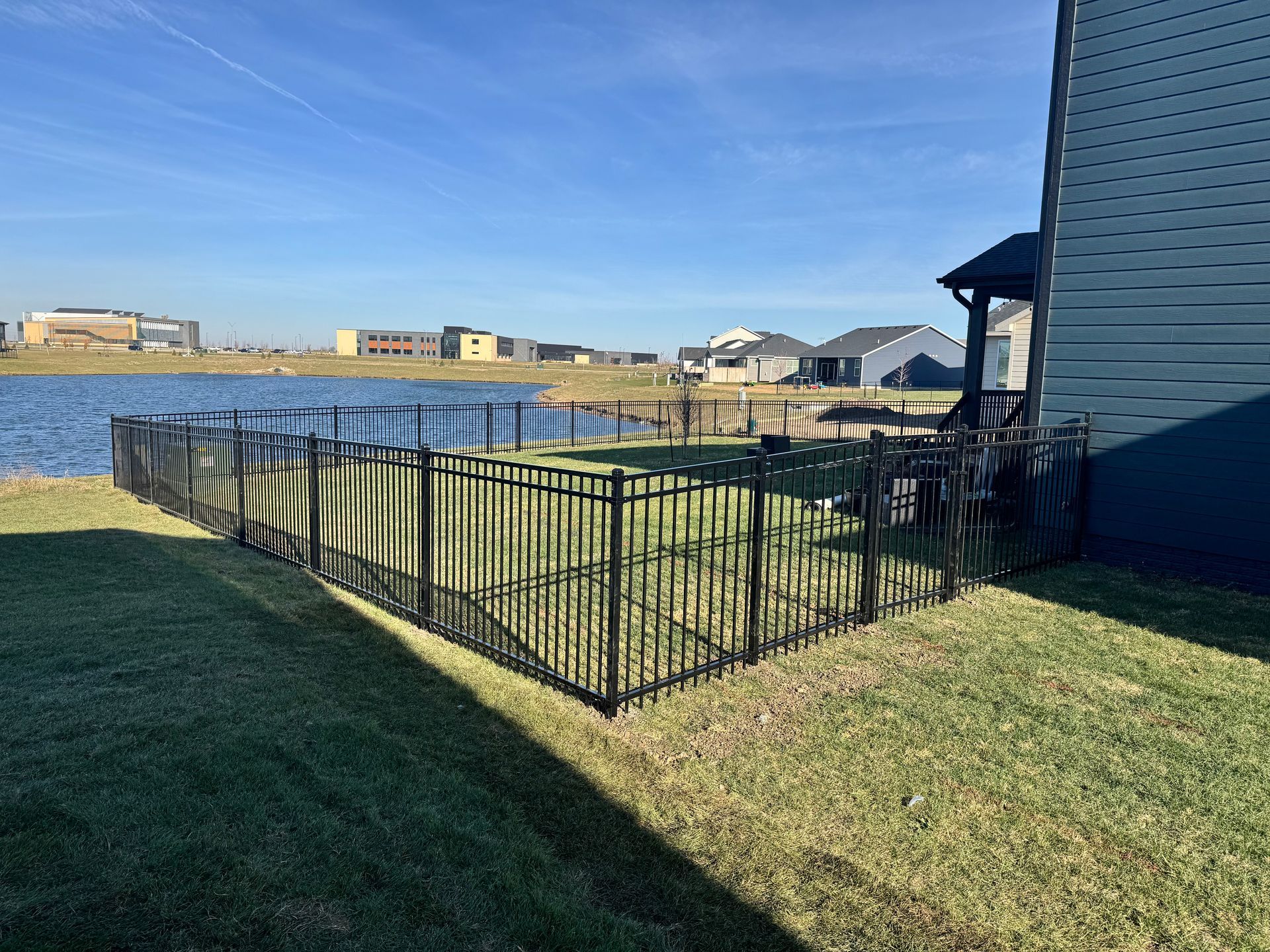 Black fence surrounds a grassy yard with a patio and trees in the background.