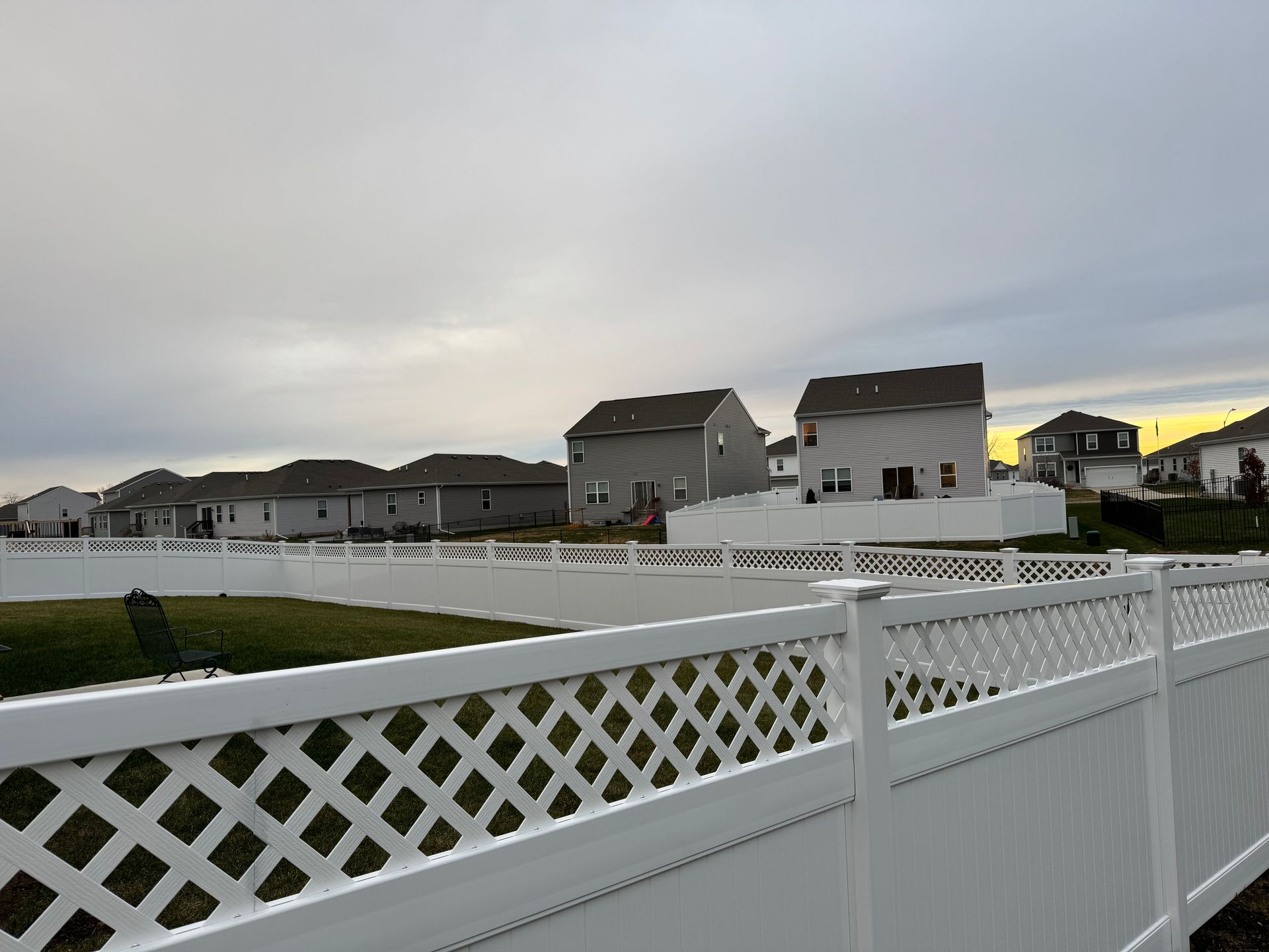 White fence along a grassy backyard under a blue sky, trees in the distance.