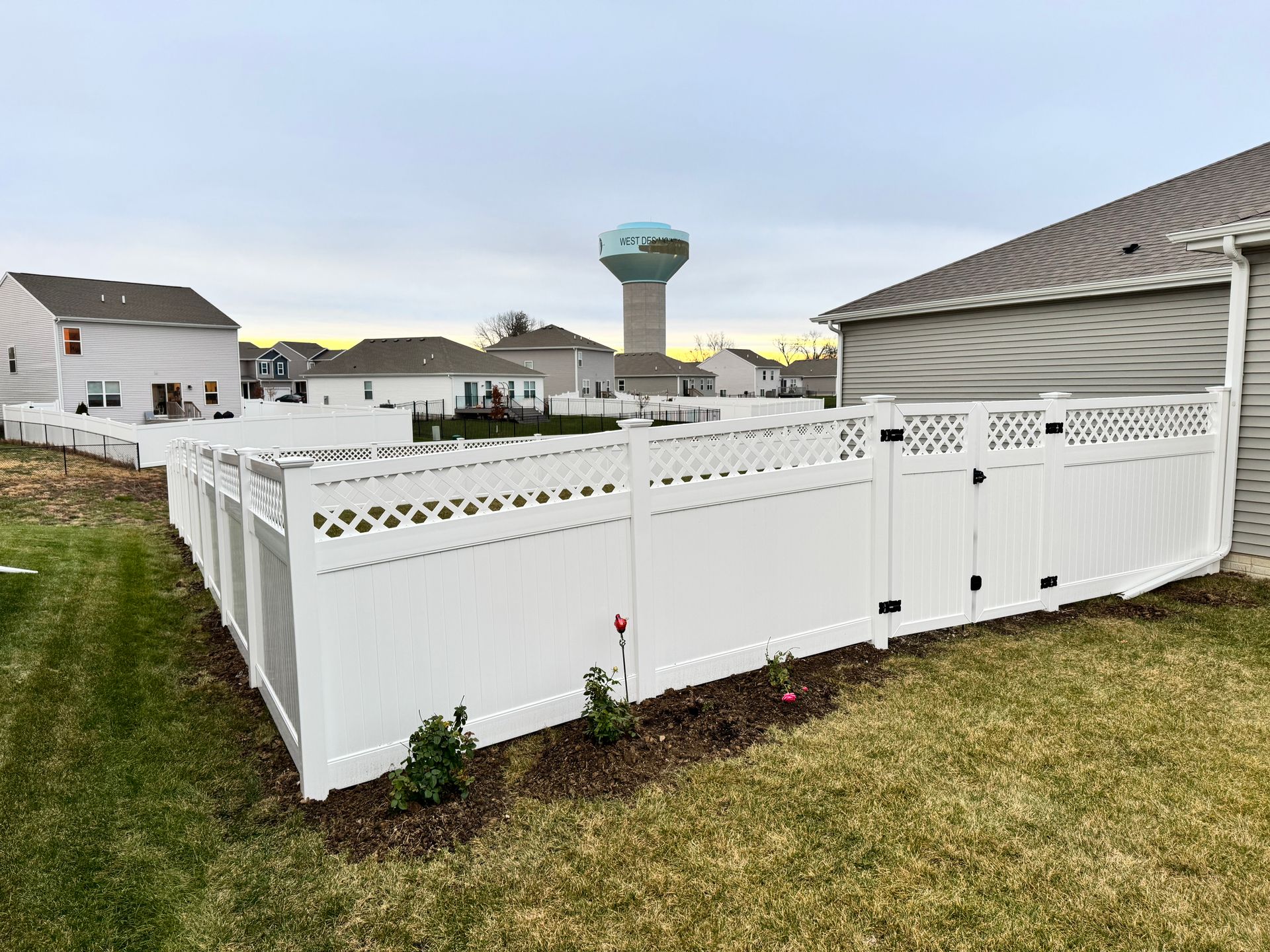 White picket fence around a pool, with a sunset over residential homes.