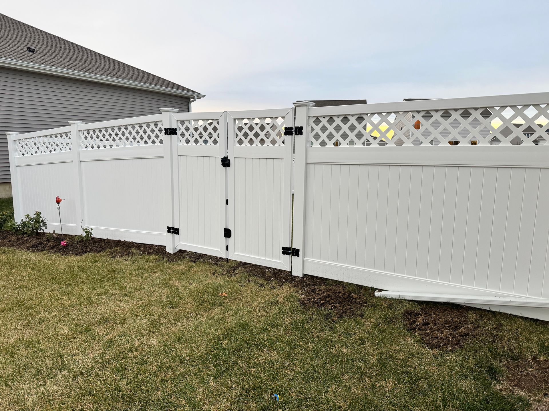 Wooden fence bordering a grassy yard with houses in the background on a cloudy day.
