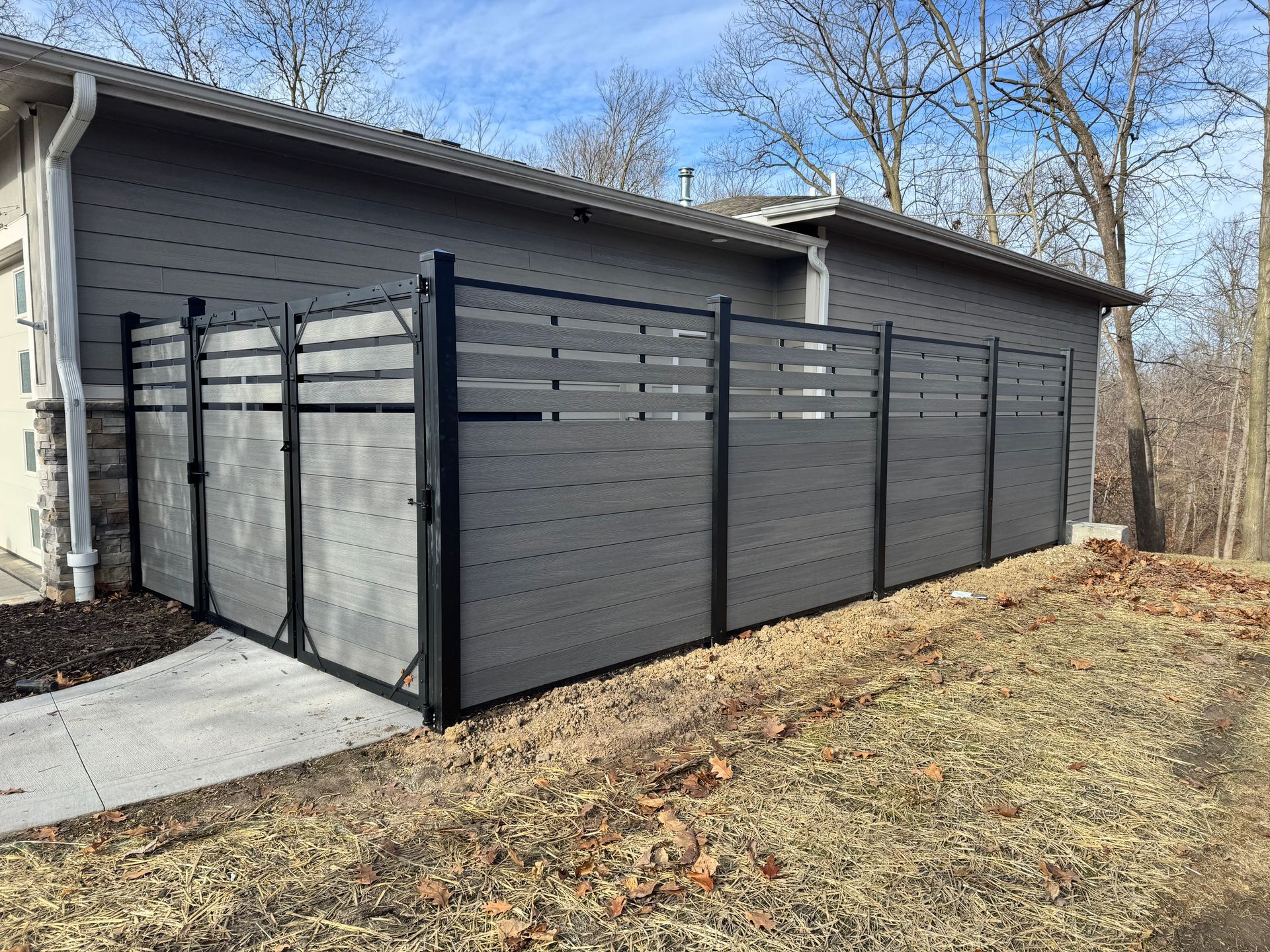 Gray privacy fence with black metal frame next to a house.