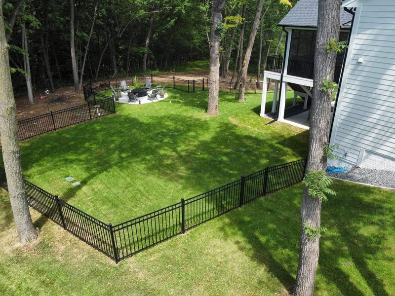 Black fenced backyard with manicured grass, a fire pit, and a house.