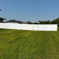 White vinyl fence in a grassy yard under a blue sky, with a house in the background.