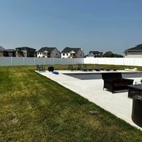 Backyard with pool, lawn, and fence; houses in the background.