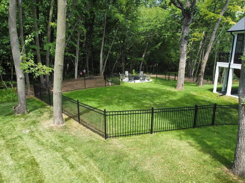 Black metal fence encloses a green lawn in a wooded area. 