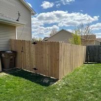 A wooden fence in a grassy backyard with a beige house in the background. 