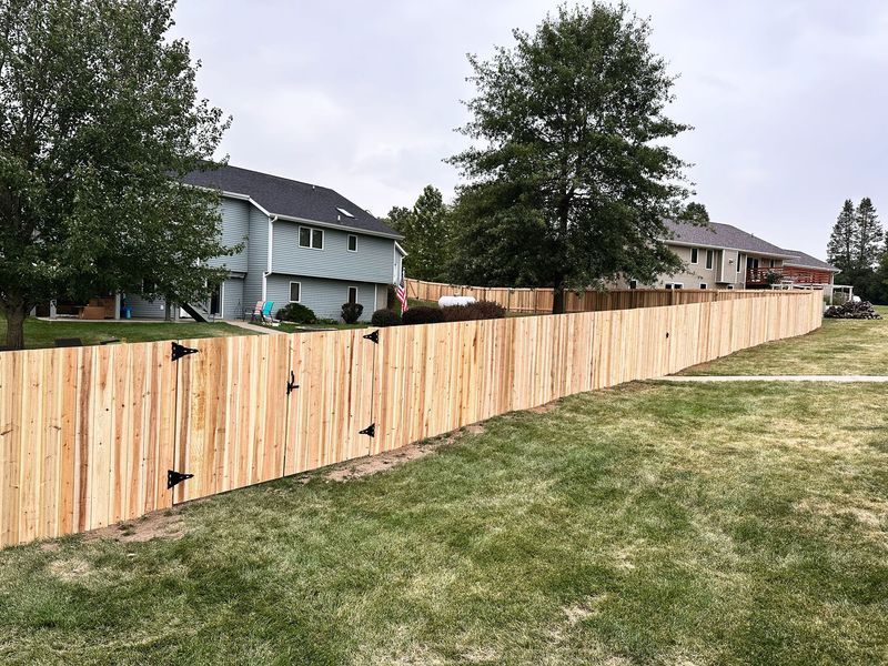 Wooden fence bordering a grassy yard with houses in the background on a cloudy day.