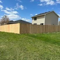 Wooden fence in front of a house on a grassy lawn under a blue sky.