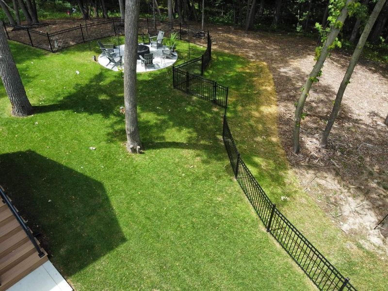 Lush green backyard with black fence, fire pit, and trees. 