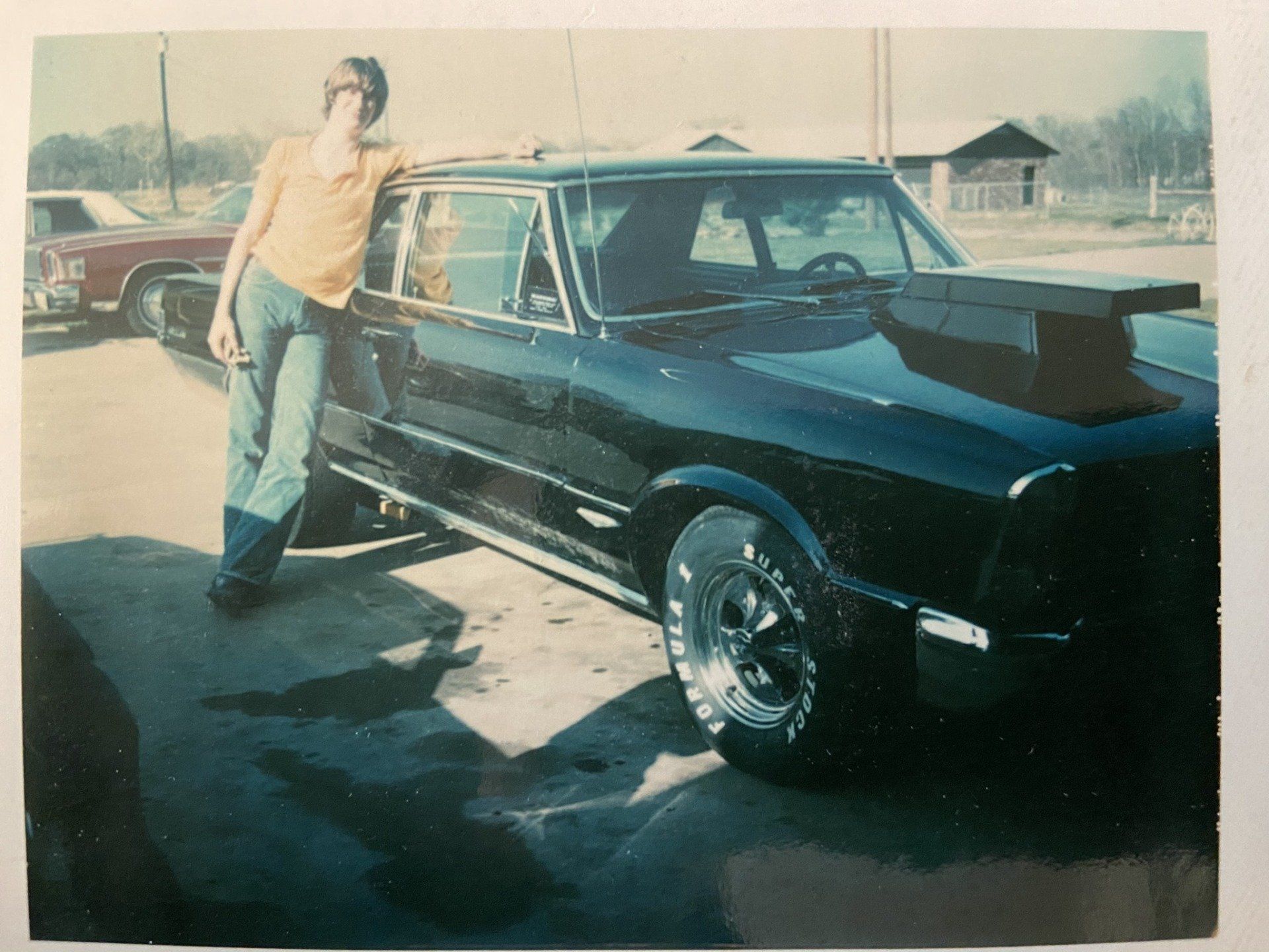 A man in a yellow shirt is standing next to a black car