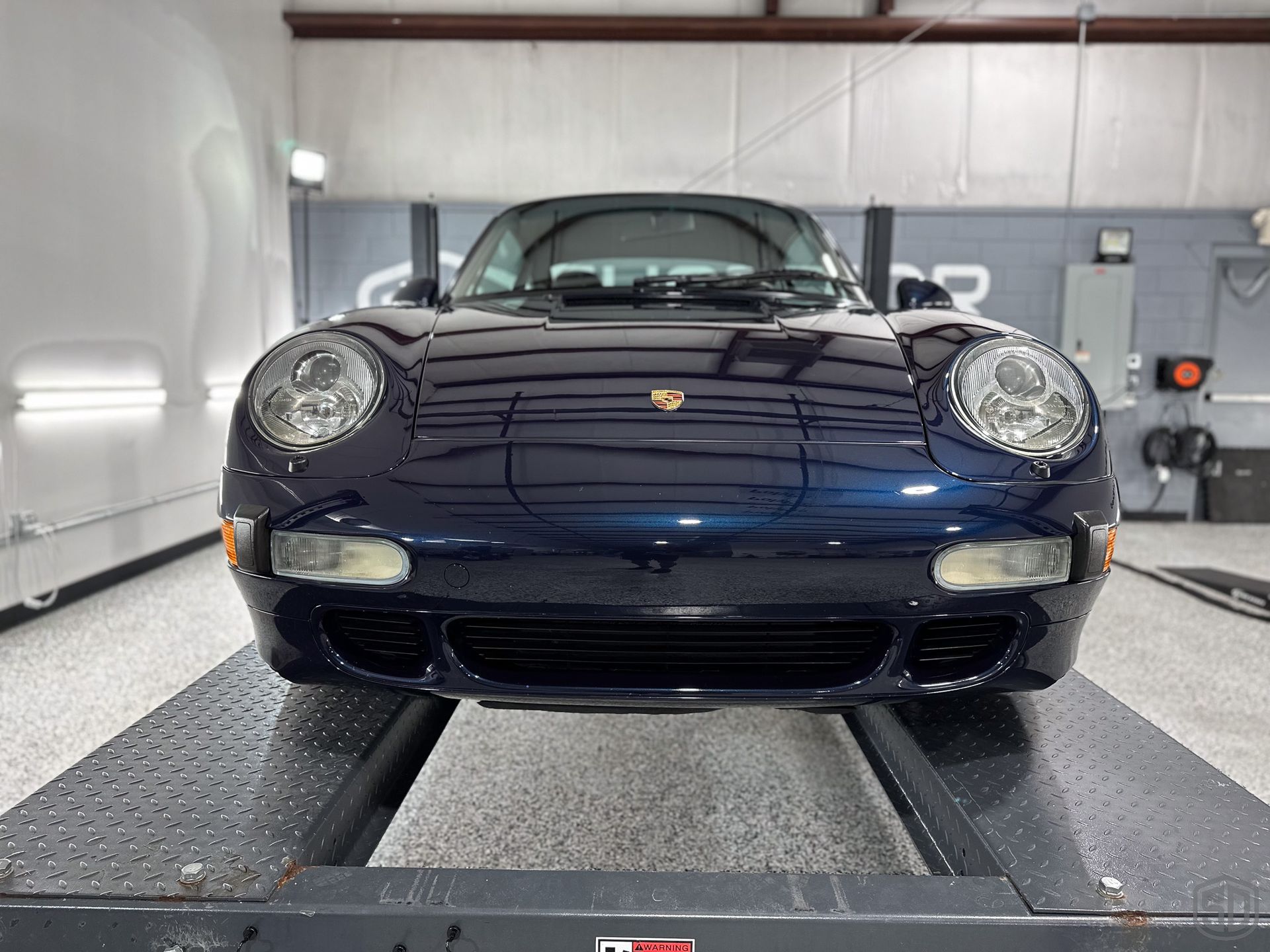 A blue porsche 911 is sitting on a lift in a garage.