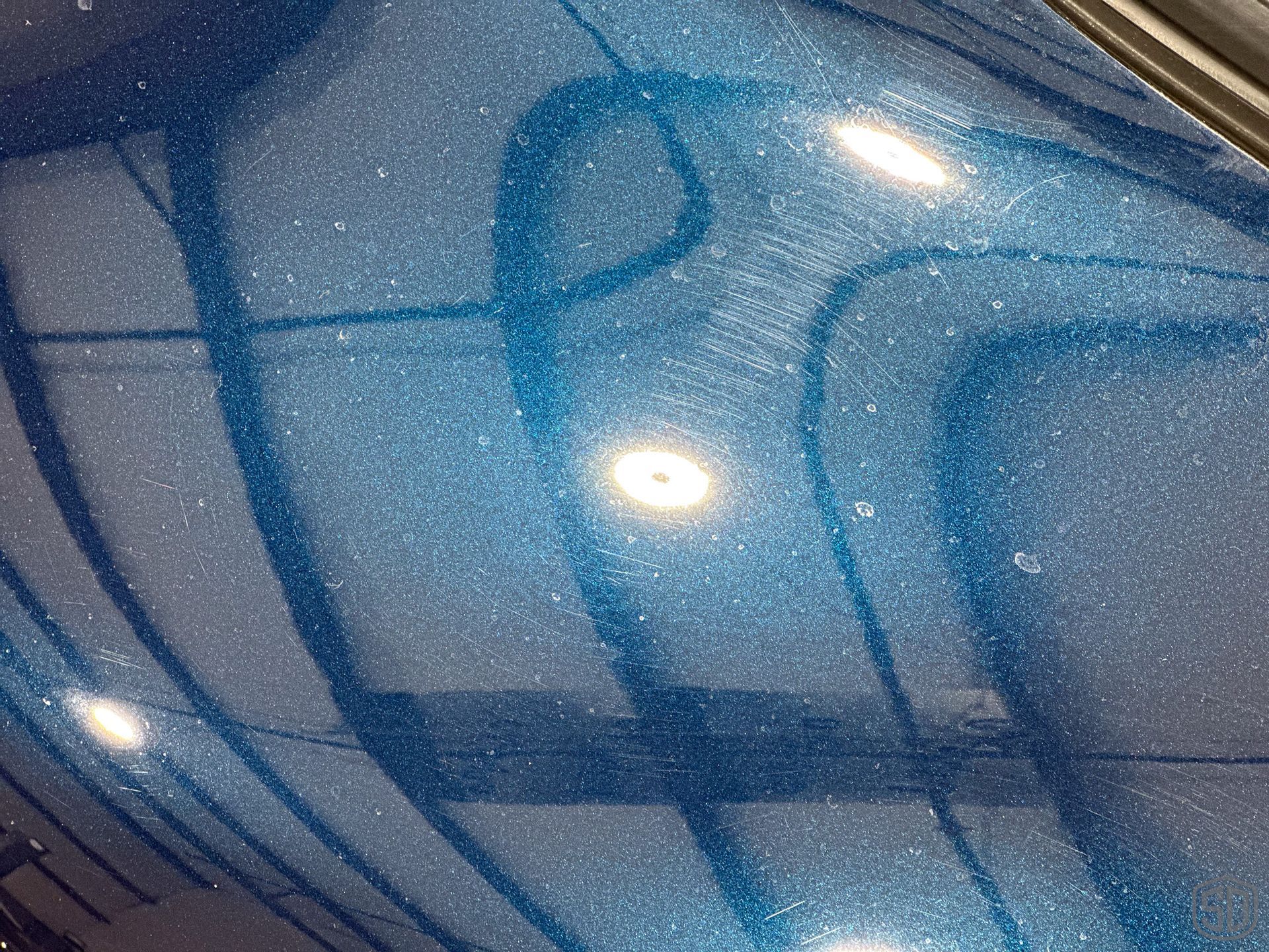 A close up of a blue shiny surface with a reflection of a car
