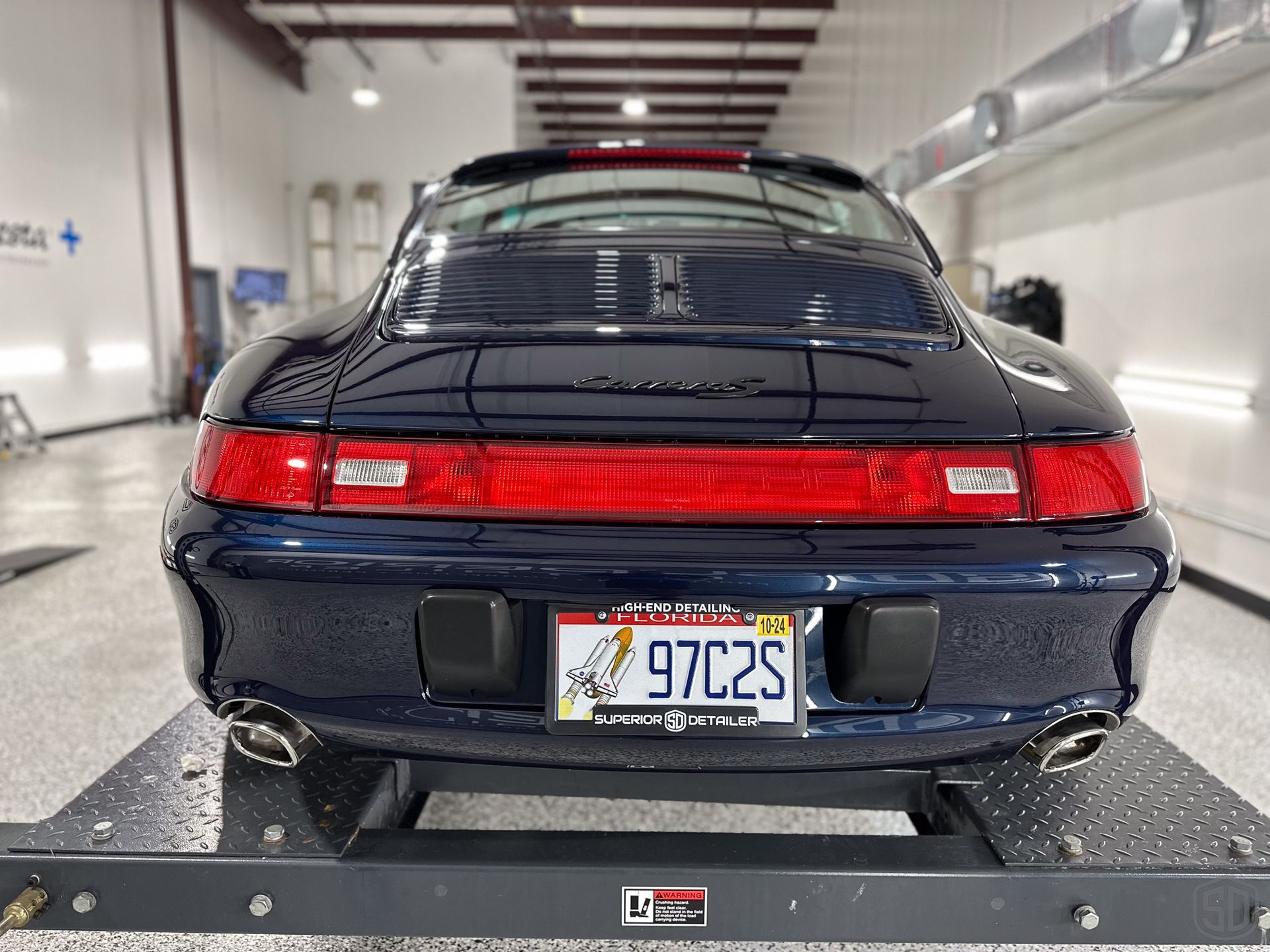 A black porsche 911 is sitting on a scale in a garage.