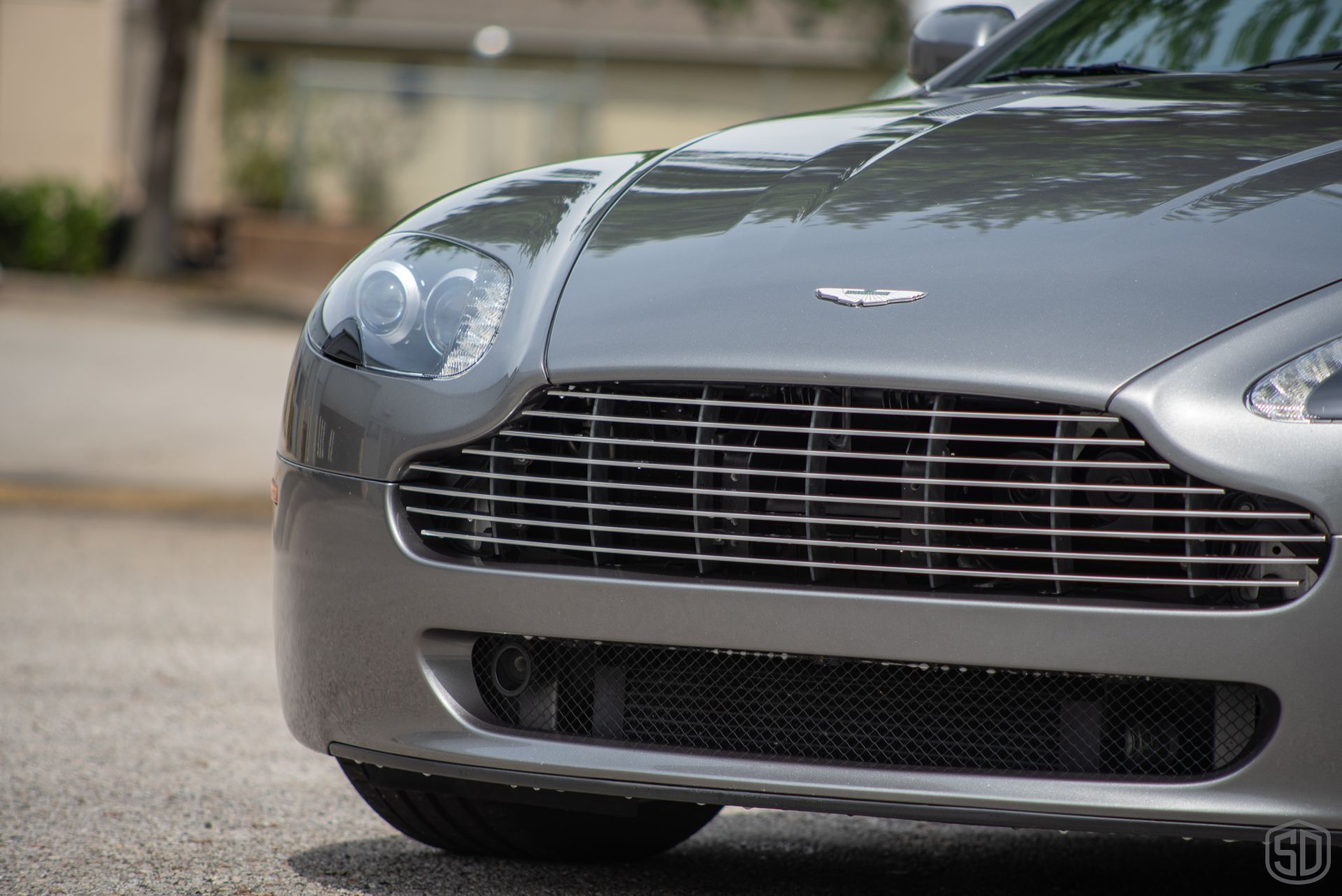 A close up of the front of a silver sports car parked on the side of the road.