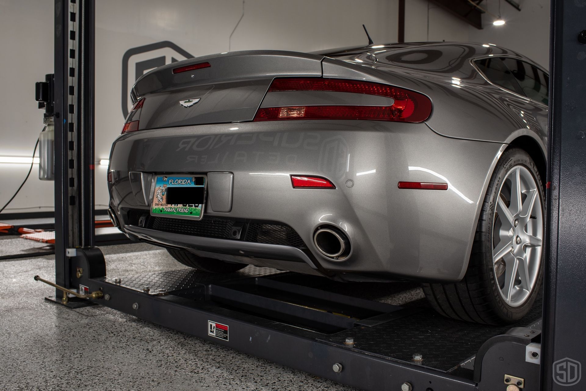 A gray sports car is on a lift in a garage.